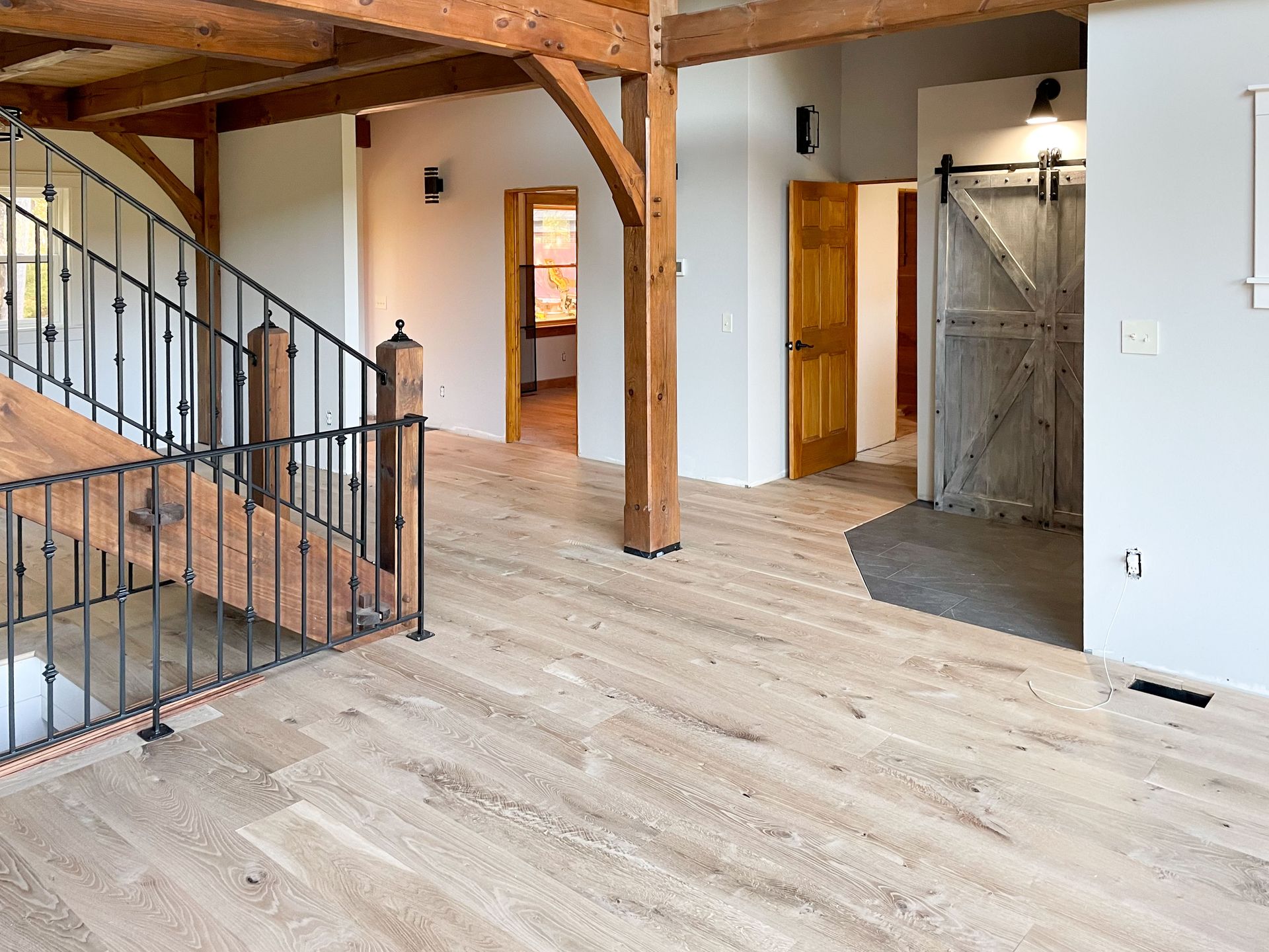 Interior with wooden beams, light wood floors, staircase, and open doorways.
