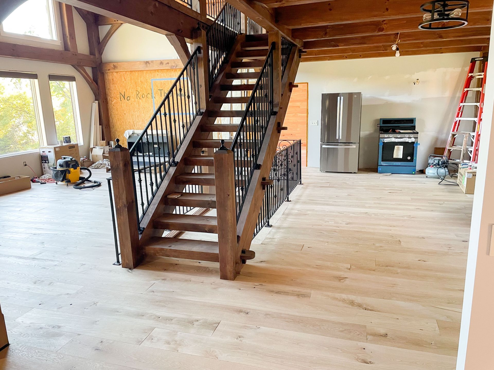 Interior of a house under construction; a wooden staircase with black iron railings dominates the room.