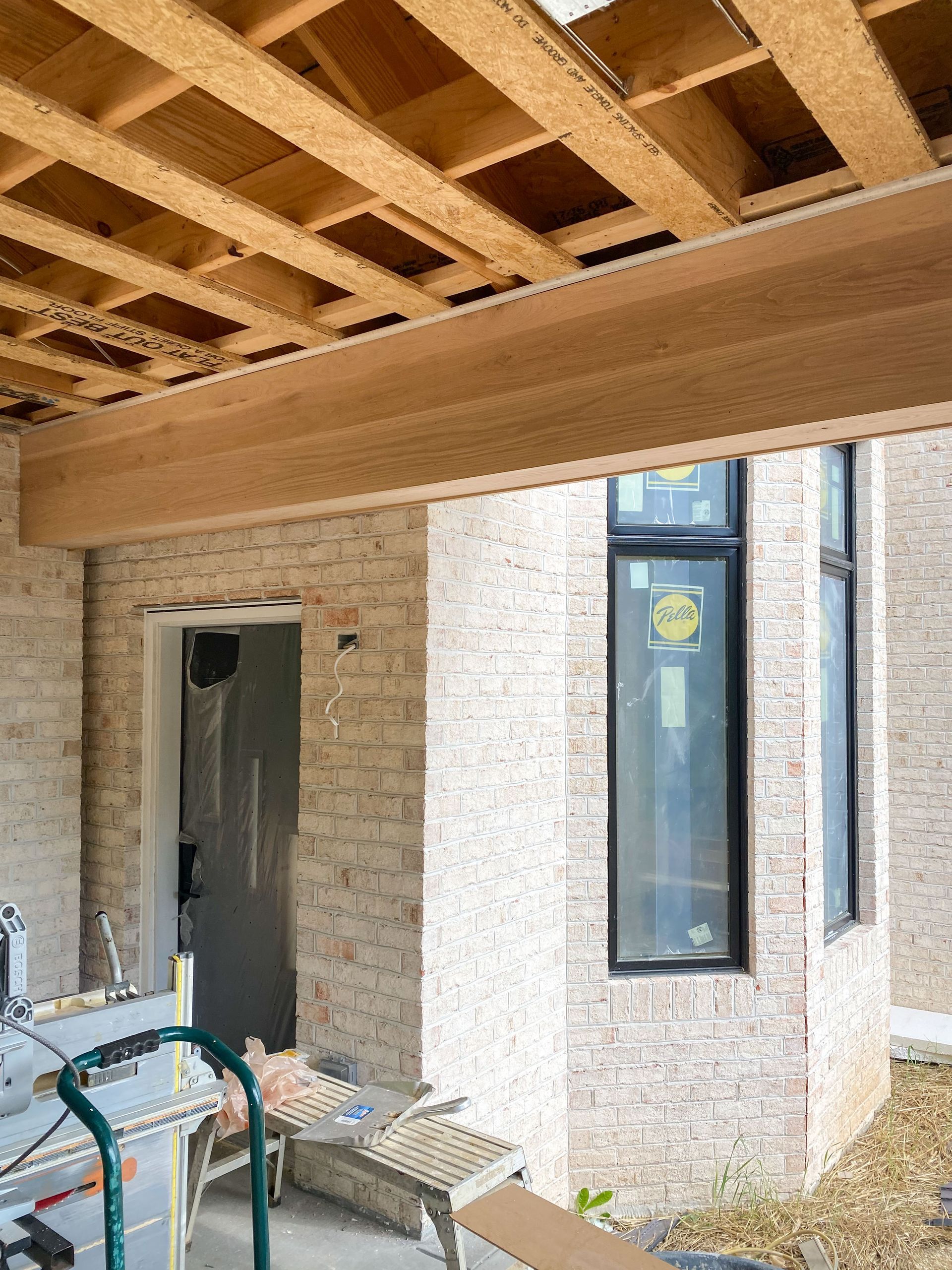 Construction site with brick wall, wood beam, and window under a wood-framed ceiling.