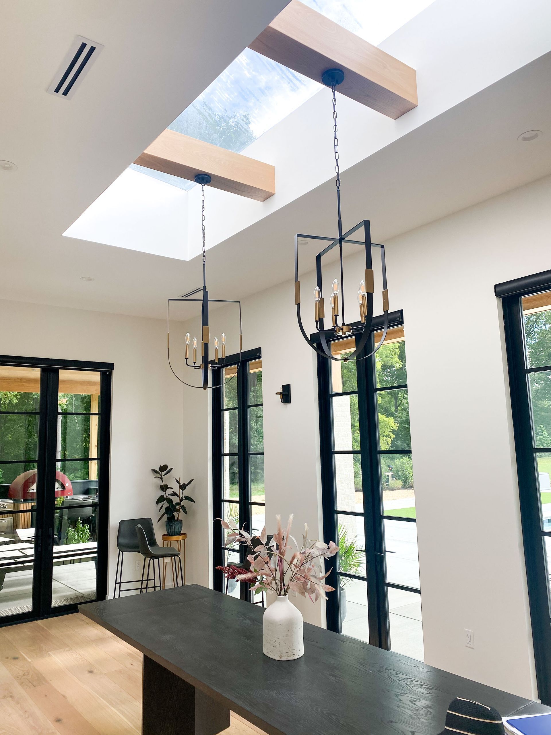 Dining room with skylight, black framed windows, dark table, hanging lights.