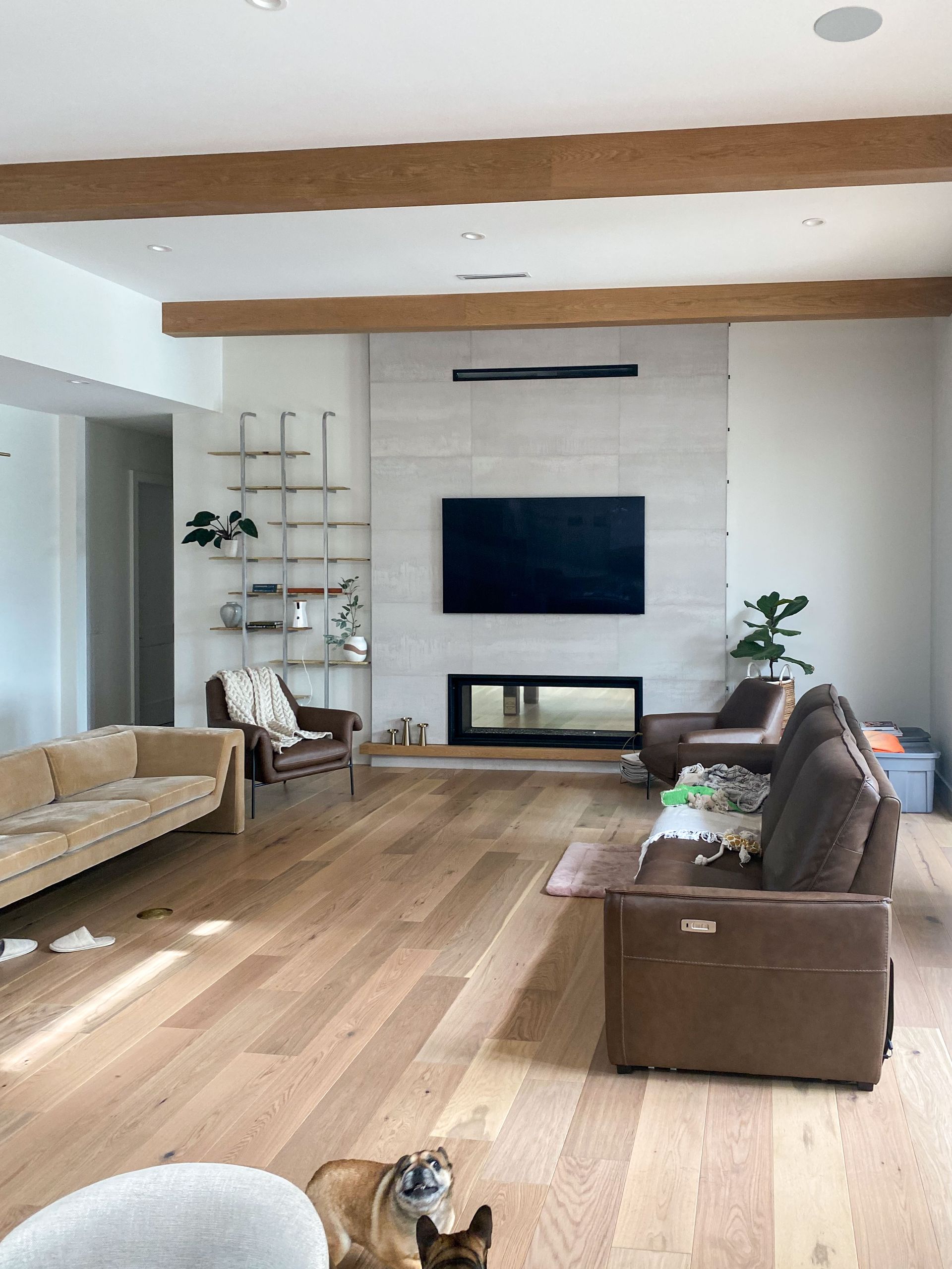 Living room with light wood floors, tan sofa, brown chairs, and a fireplace with a large TV above.