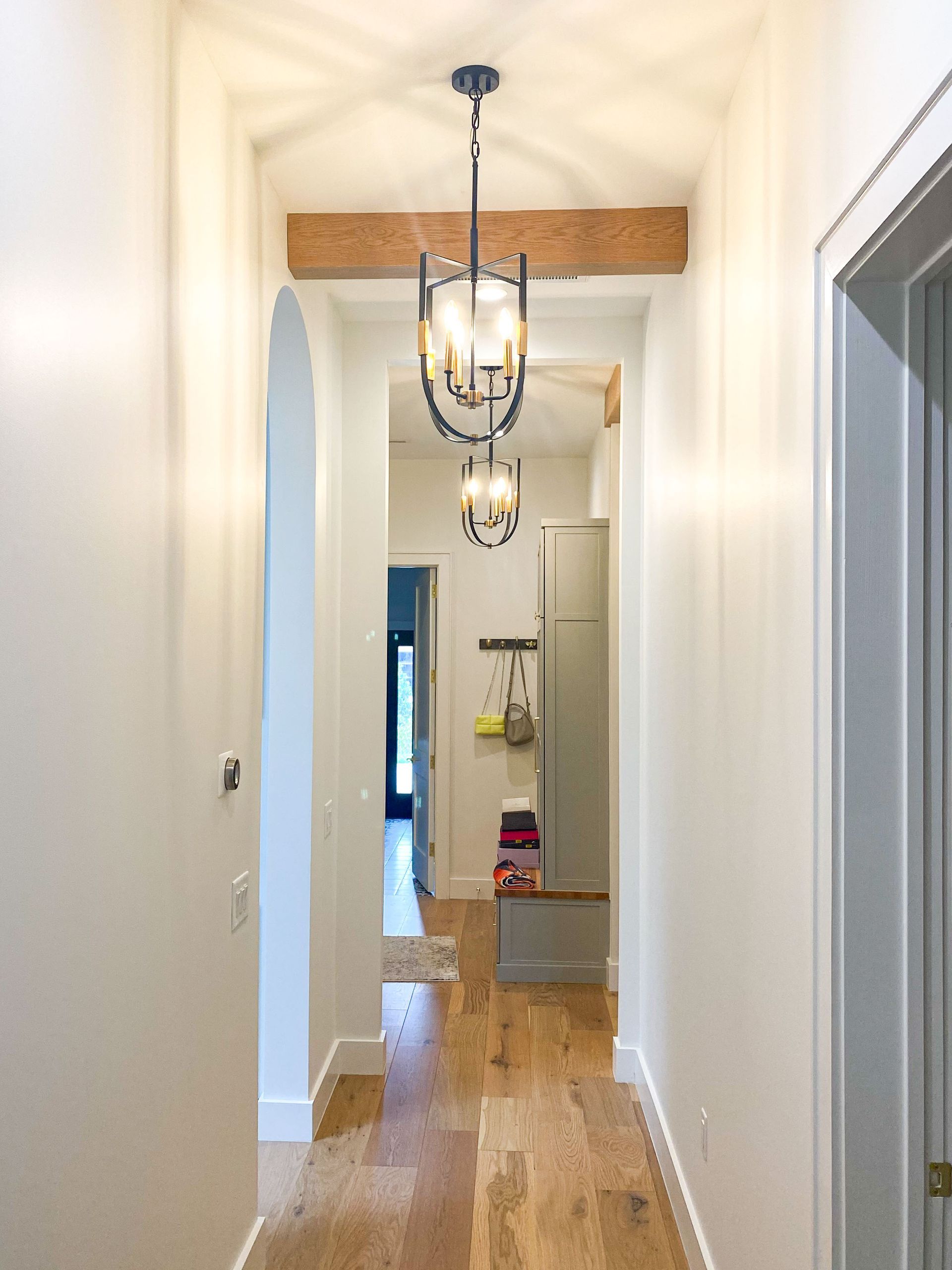 Hallway with wooden floor, white walls, arched doorway, and decorative hanging lights.