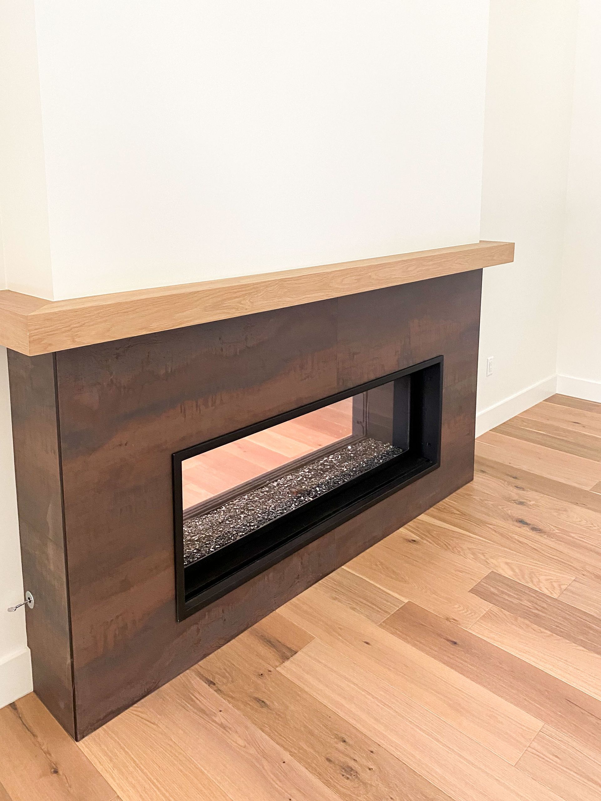Built-in fireplace with dark wood surround, black frame, and stones, set against a white wall and wood flooring.