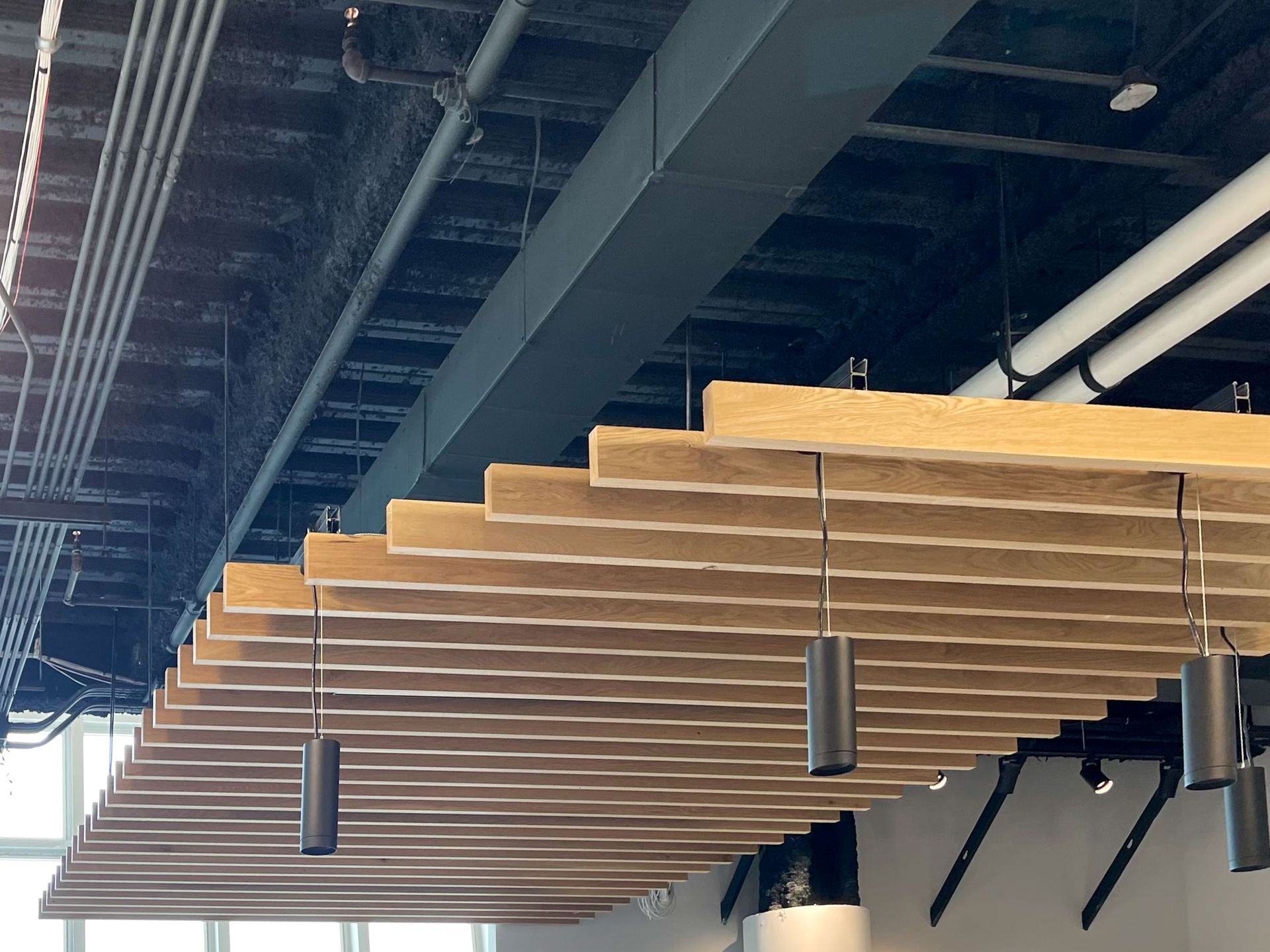 Rows of light brown, slat-like acoustic panels hang from a black ceiling, with suspended black lights.