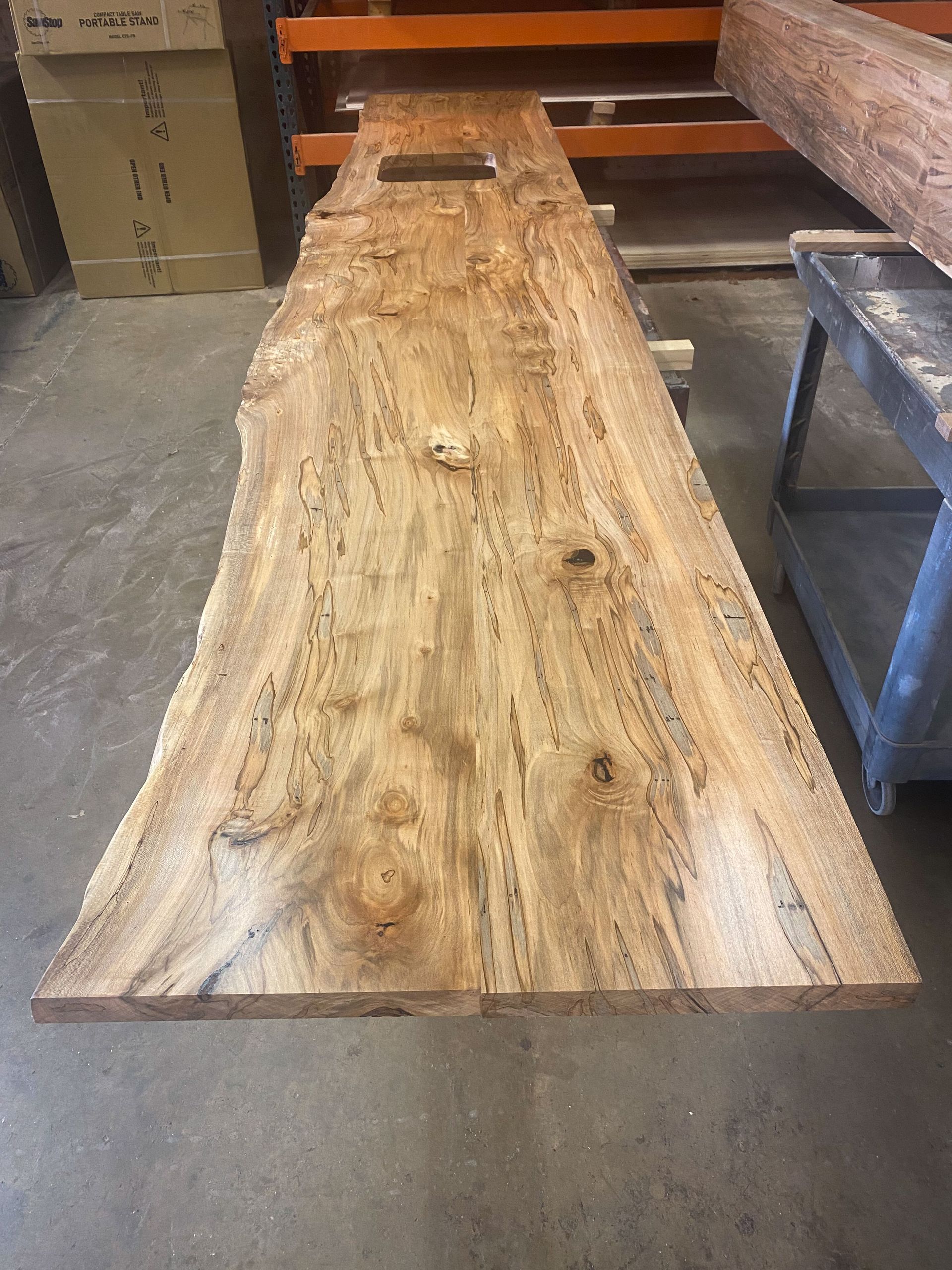 Live edge wood slab with natural edges, light brown, with knot detail.