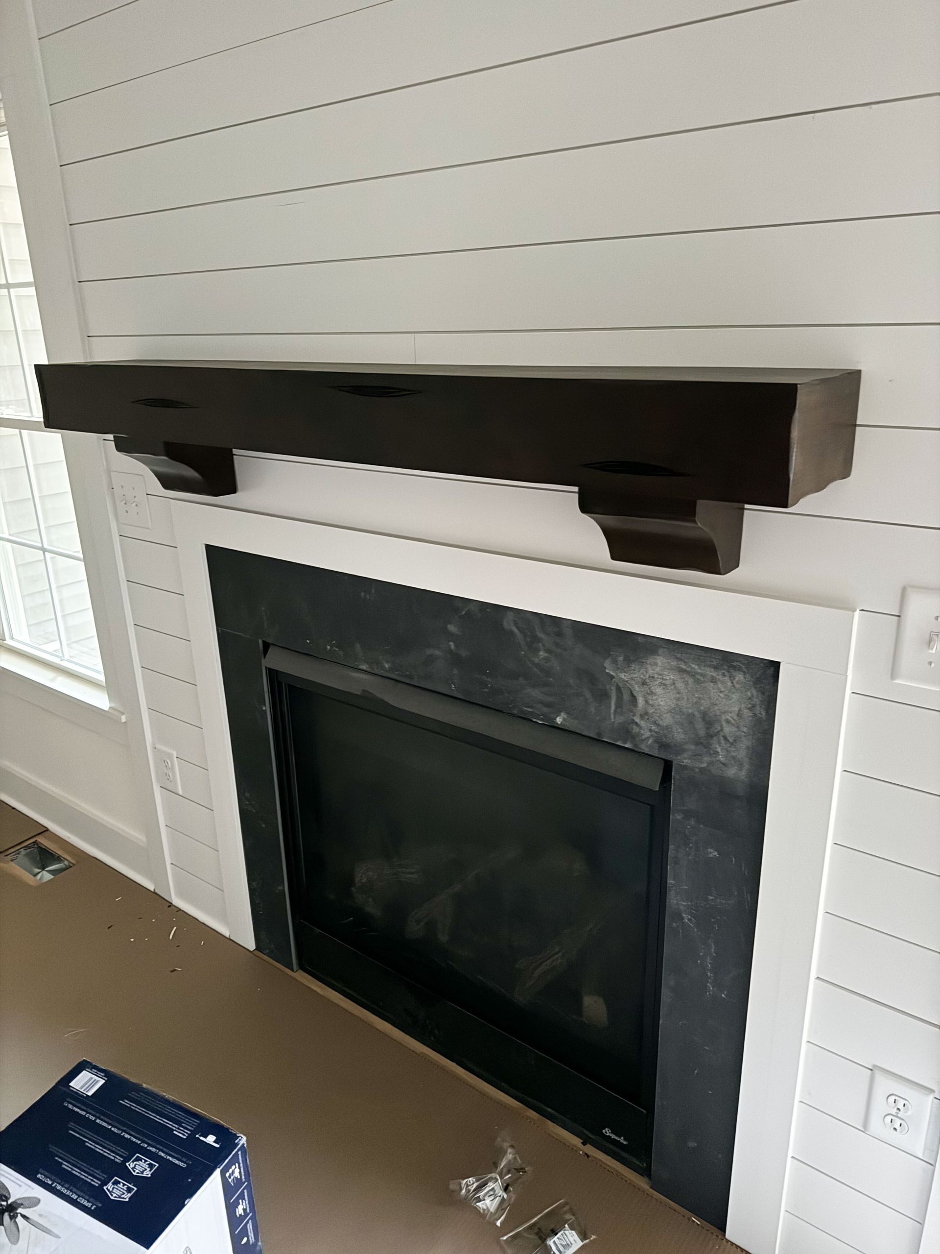 Fireplace with dark wooden mantel on white shiplap wall. Black fireplace surround.