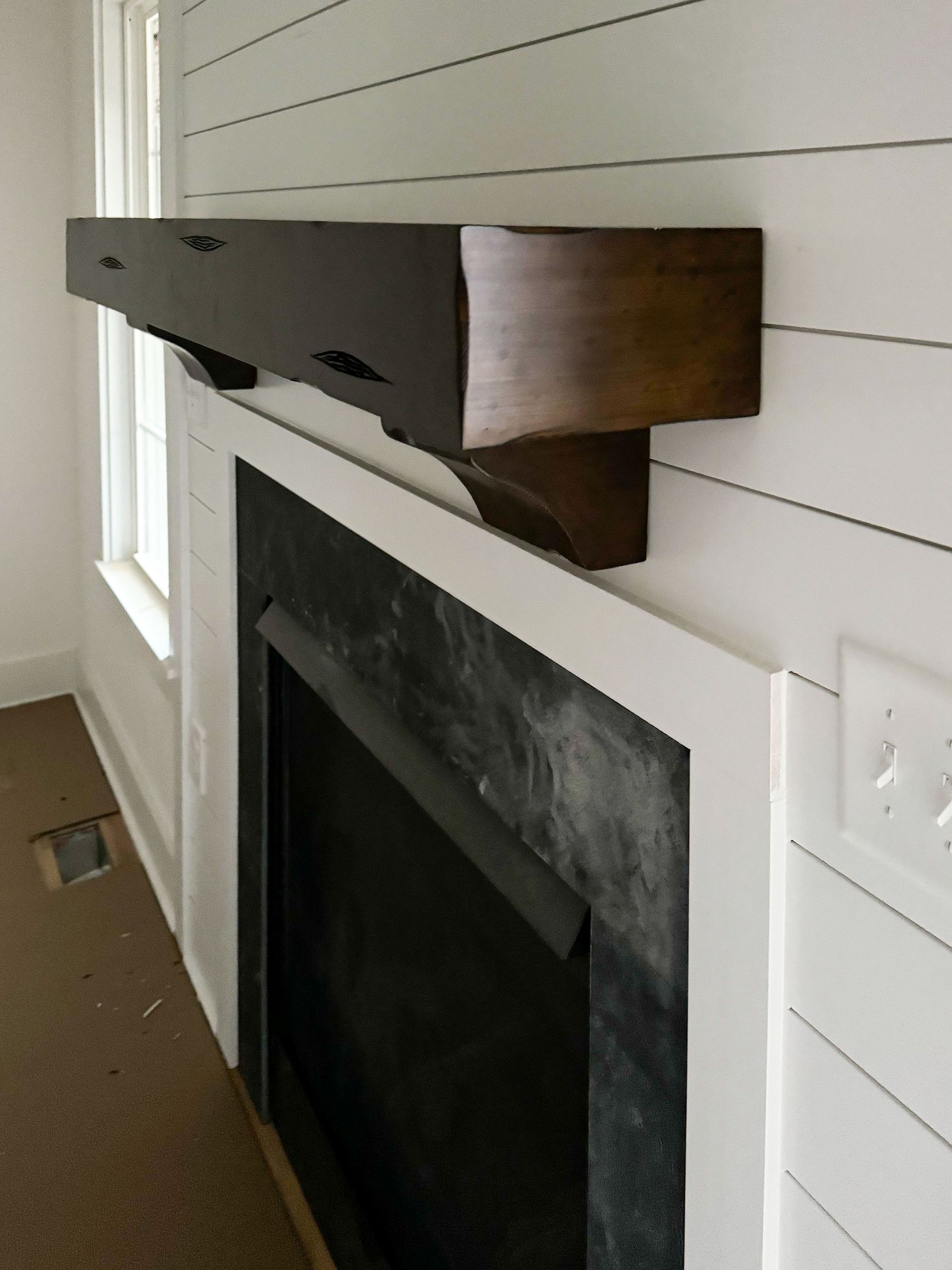Fireplace with dark wooden mantel, white trim, and shiplap wall.
