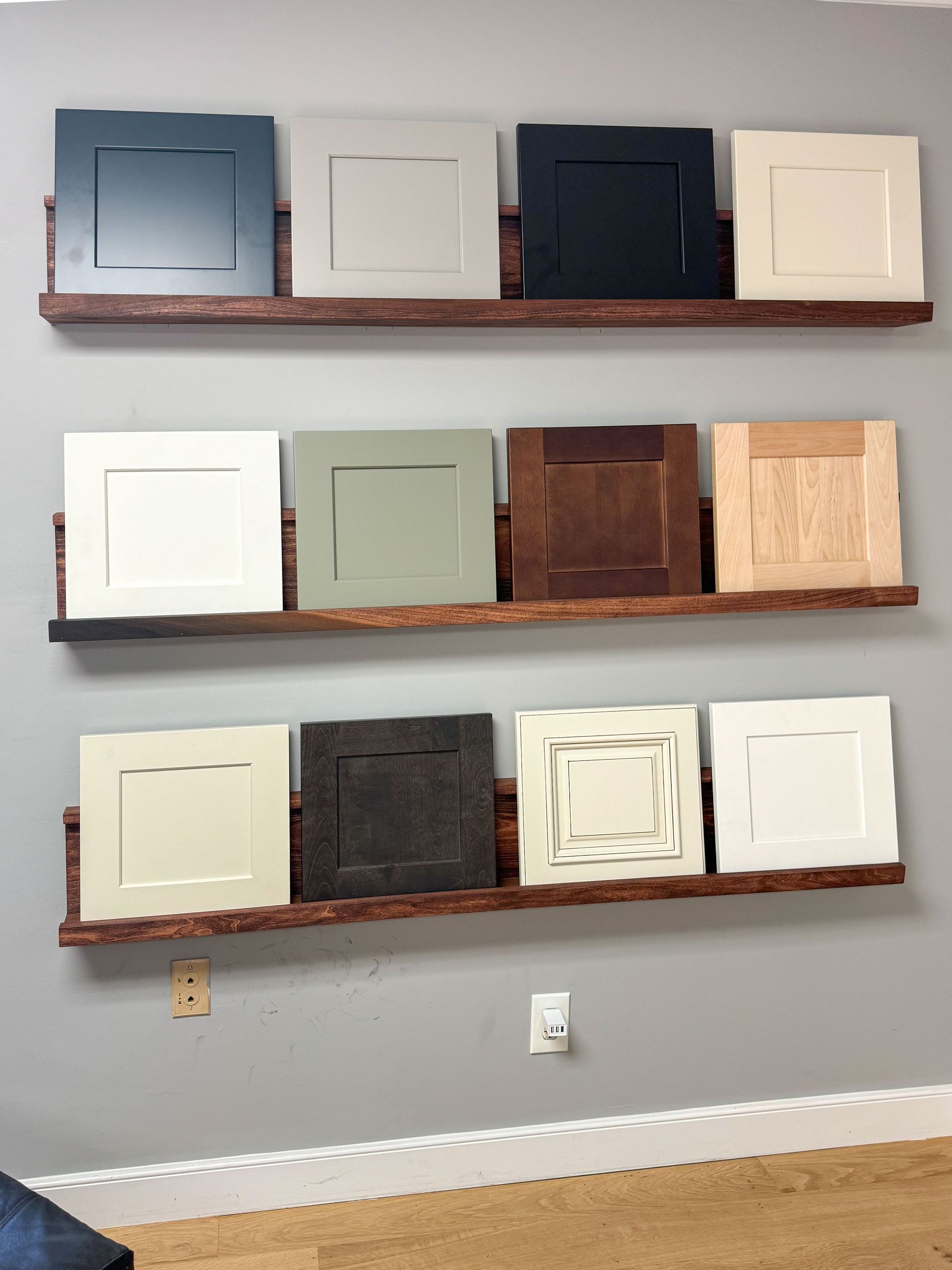 Cabinet door samples in various colors on wooden shelves against a gray wall.