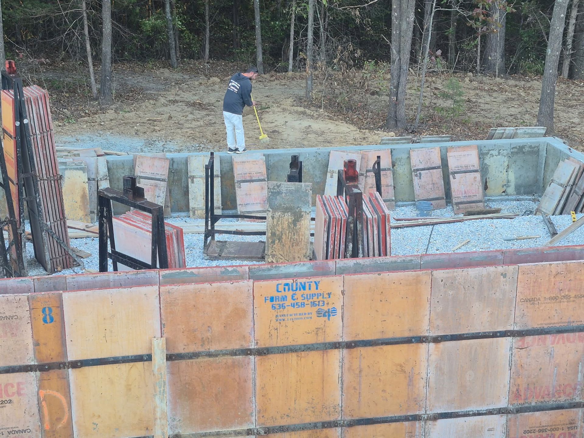 Partially built concrete foundation with stacked blocks and a worker in a wooded outdoor site