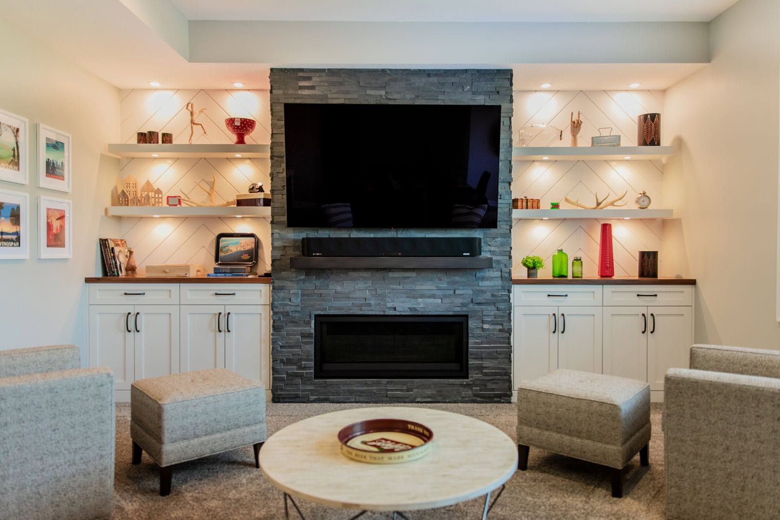 Modern living room with built-in shelves, stone fireplace, wall-mounted TV, and two chairs around a round table