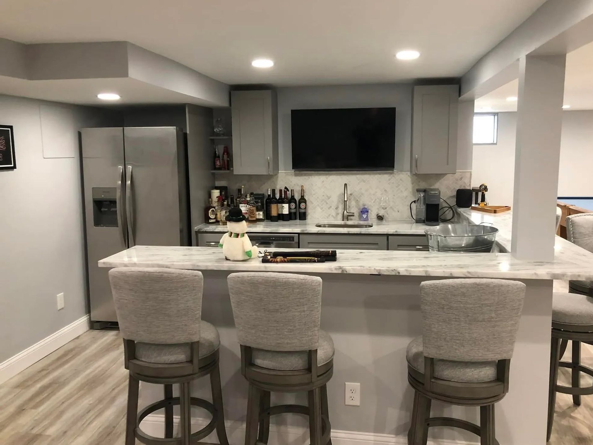 Modern gray kitchen with island, three stools, stainless fridge, and wall-mounted TV