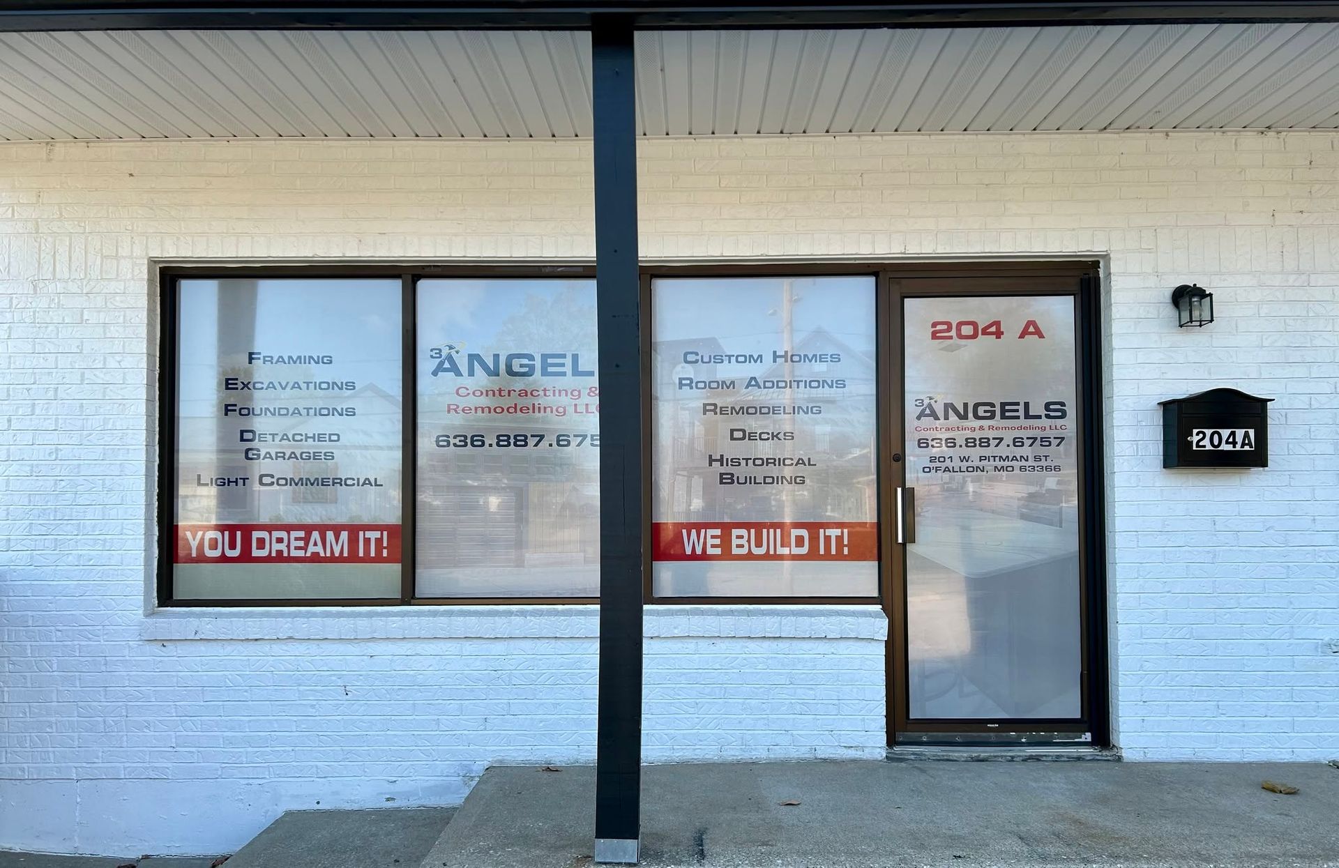 Storefront with white brick facade, black support post, and glass door/window signage for a business office.