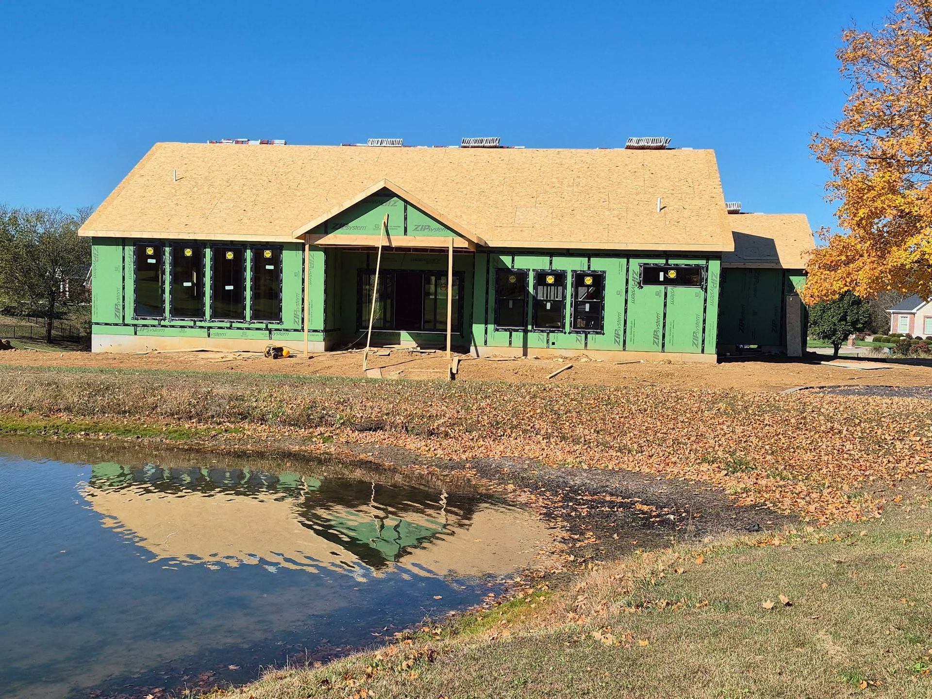 Green house with a tan roof reflected in a pond on a sunny day