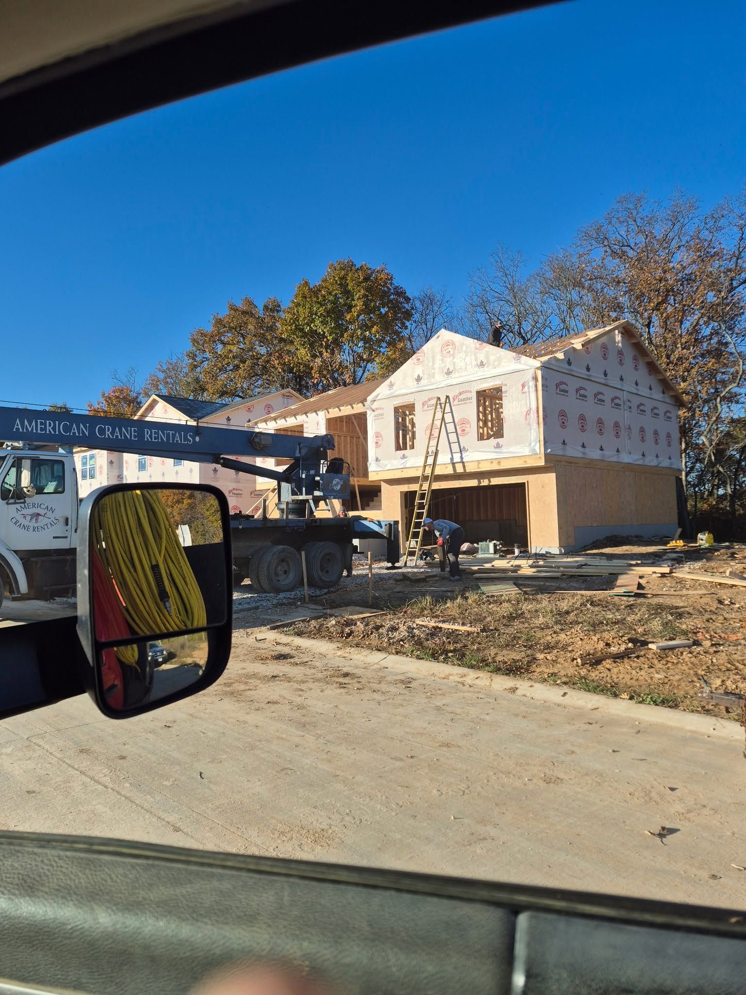 New house under construction beside a road, with a truck in the foreground and trees in the background