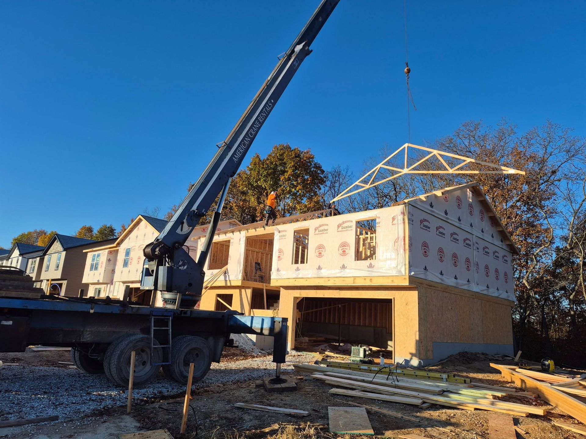 Crane lifting roof trusses at a house under construction on a sunny day