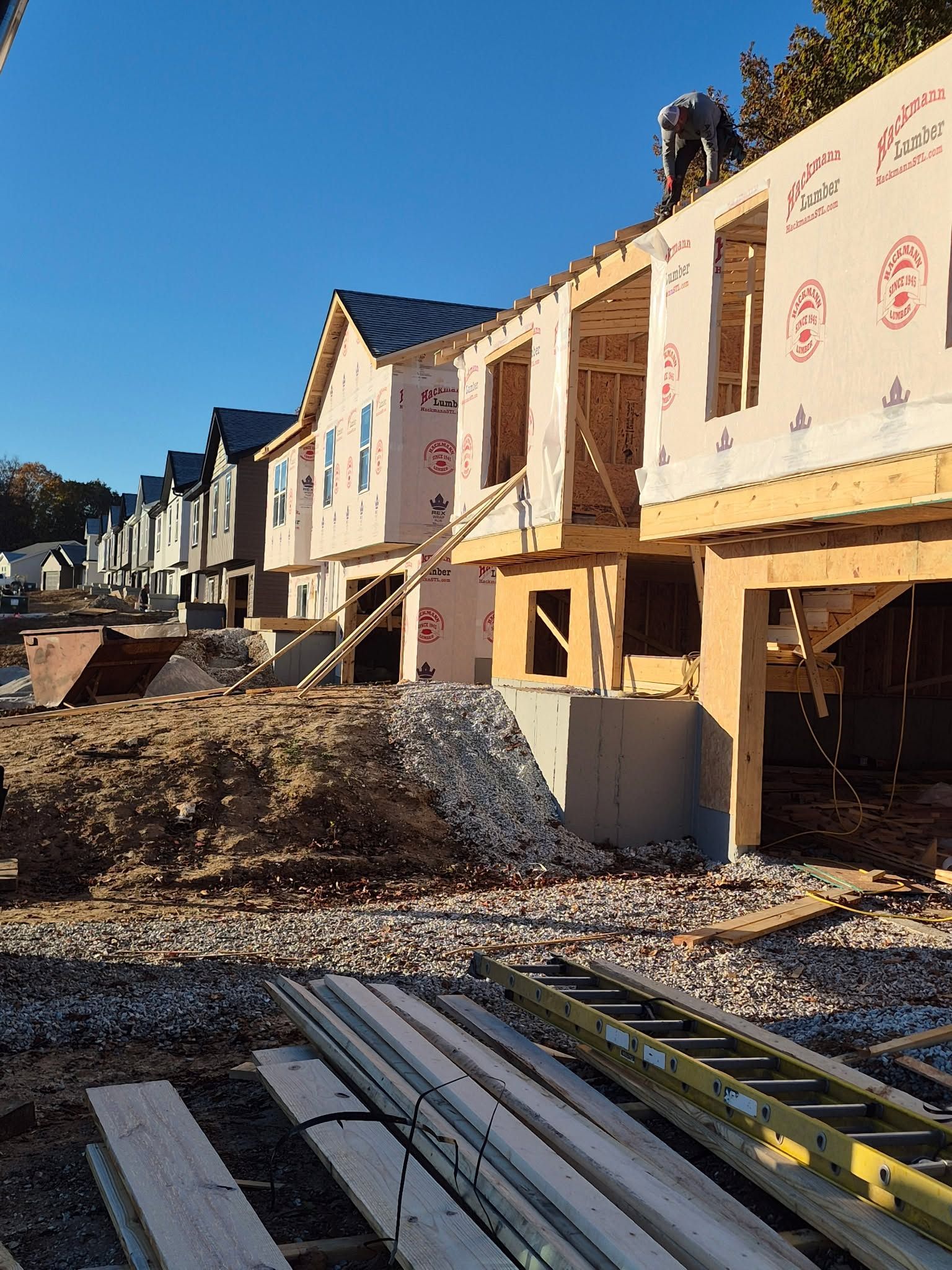 Row of unfinished townhomes under construction with exposed framing, insulation, and construction materials in front
