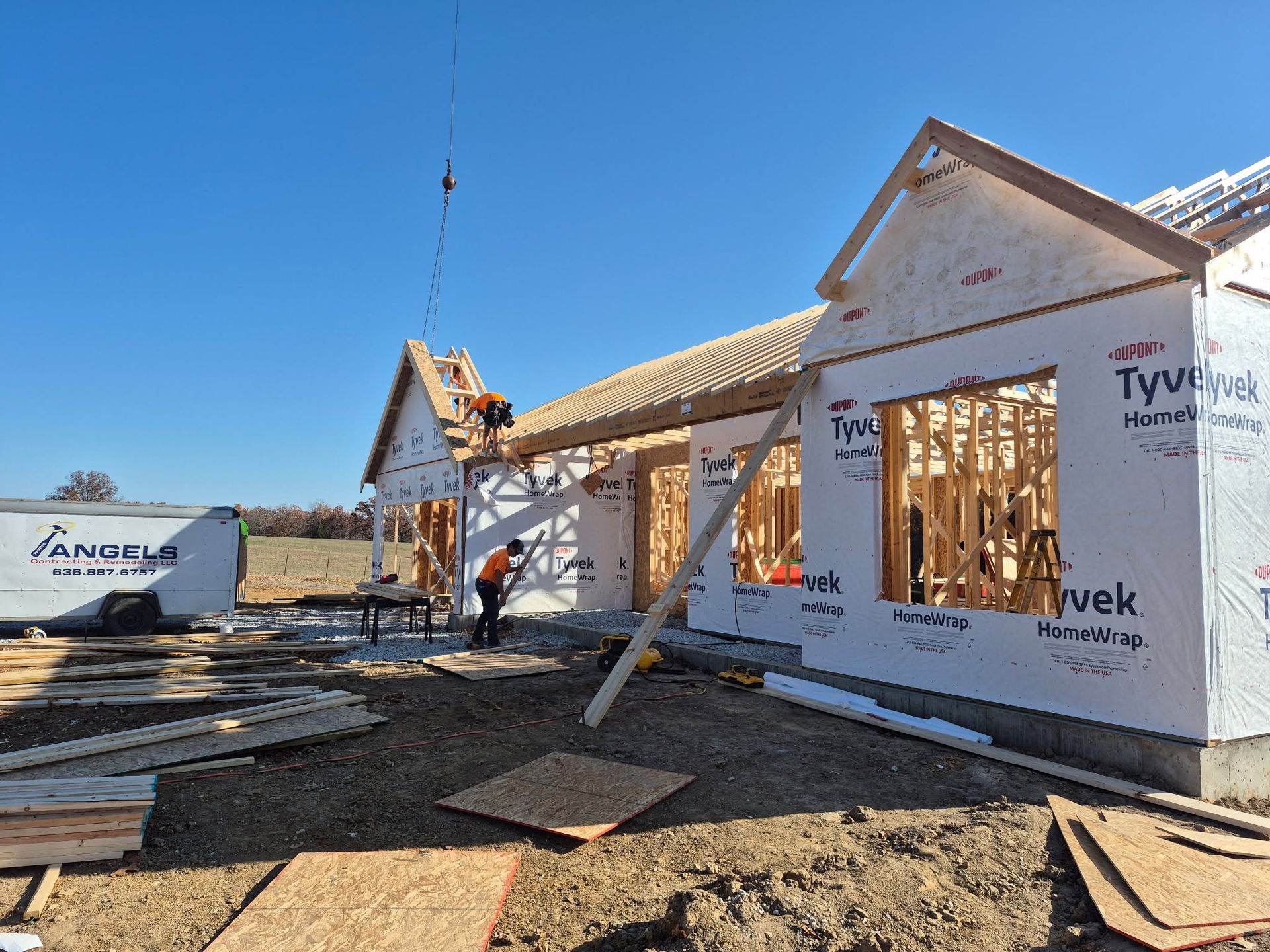 House under construction with exposed wooden framing and white exterior wrap under a clear blue sky
