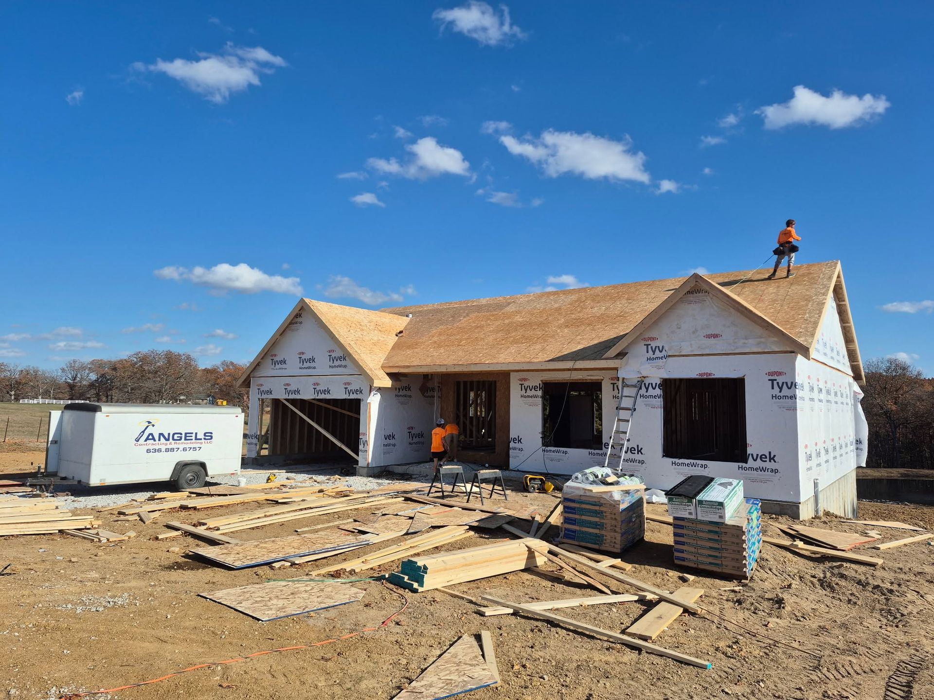 Partially built house under construction with worker on the roof and construction materials in front