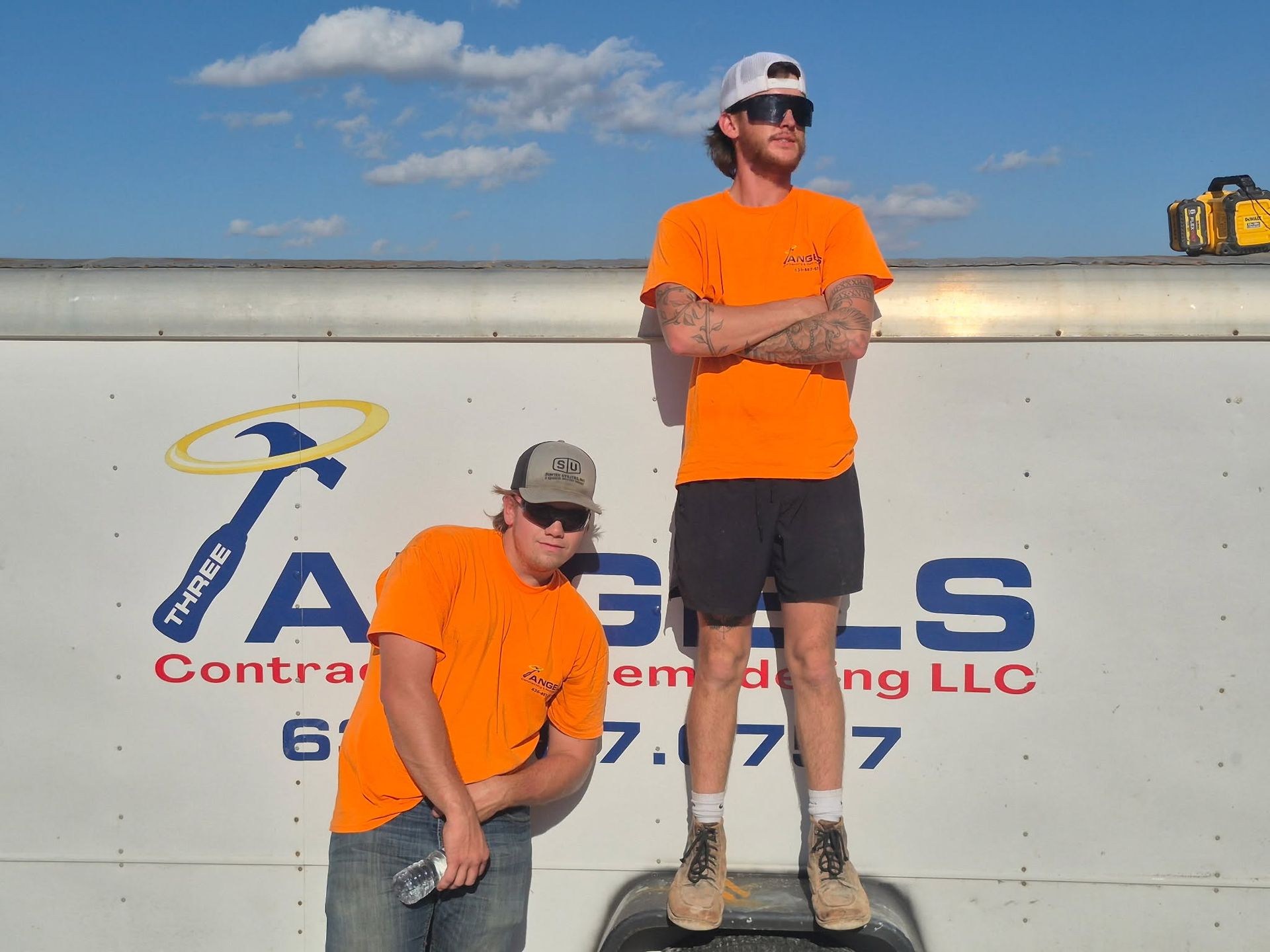 Two workers in orange shirts posing on a truck bed in front of a company logo.