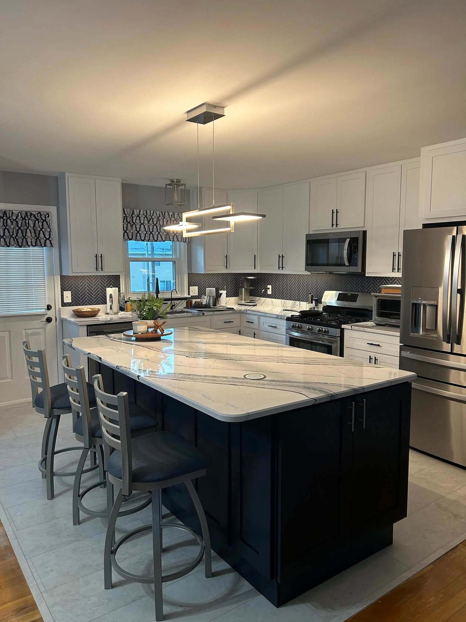 Modern kitchen with a large island, stainless steel appliances, and three stools under pendant lights
