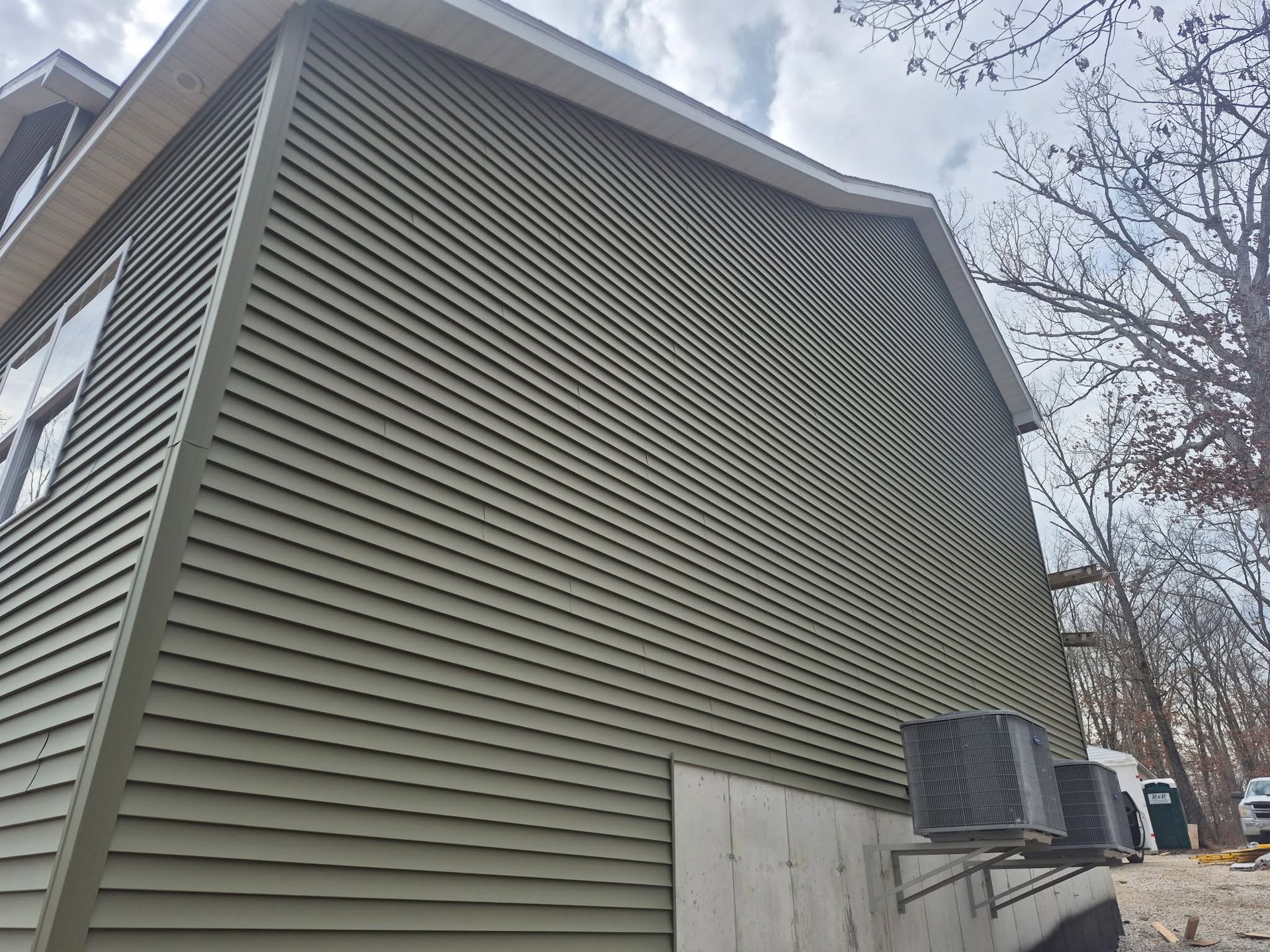 Side view of a green house with vinyl siding and two air conditioning units beside it