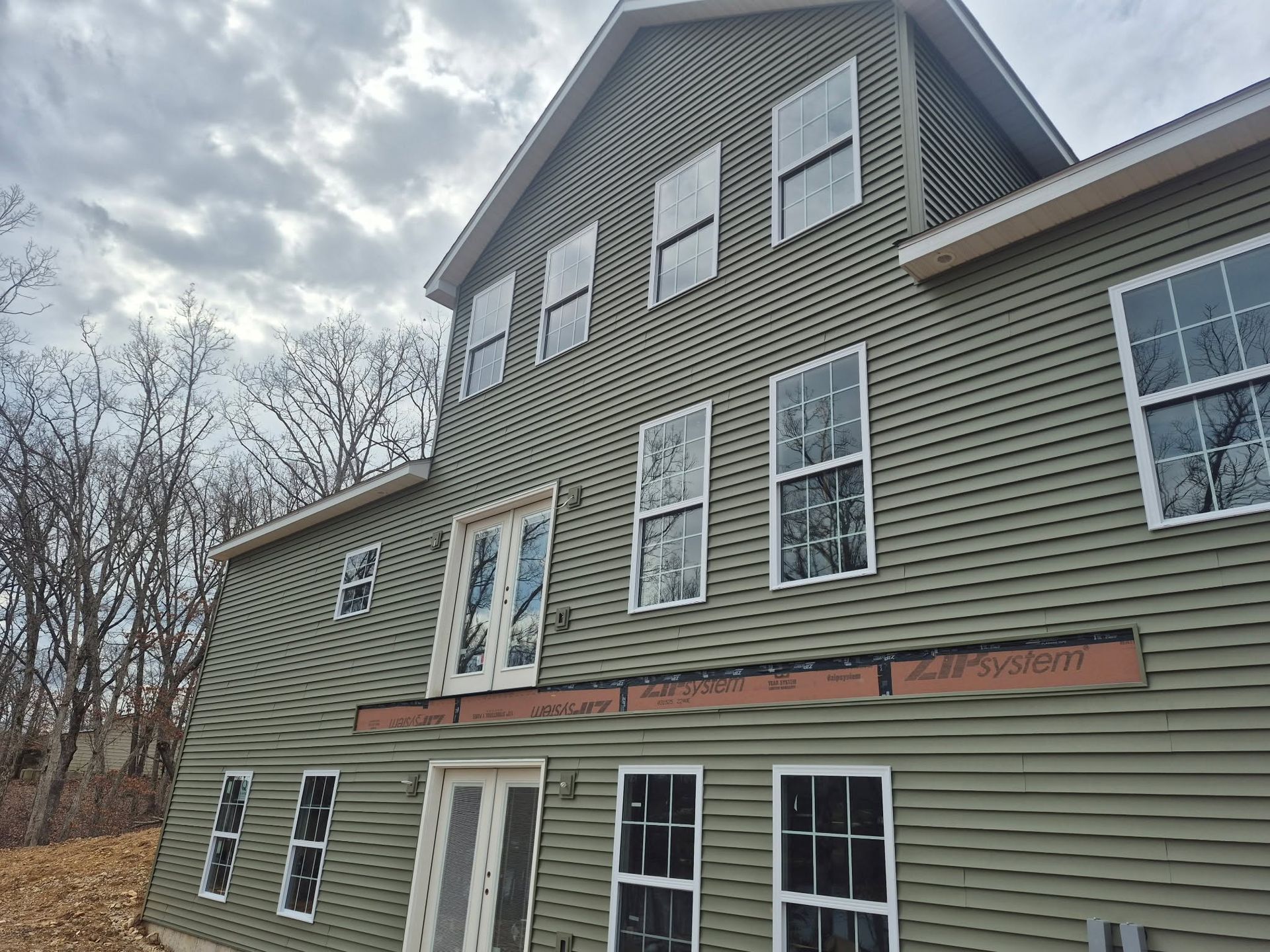 Three-story gray house with white trim and a cloudy sky above it.