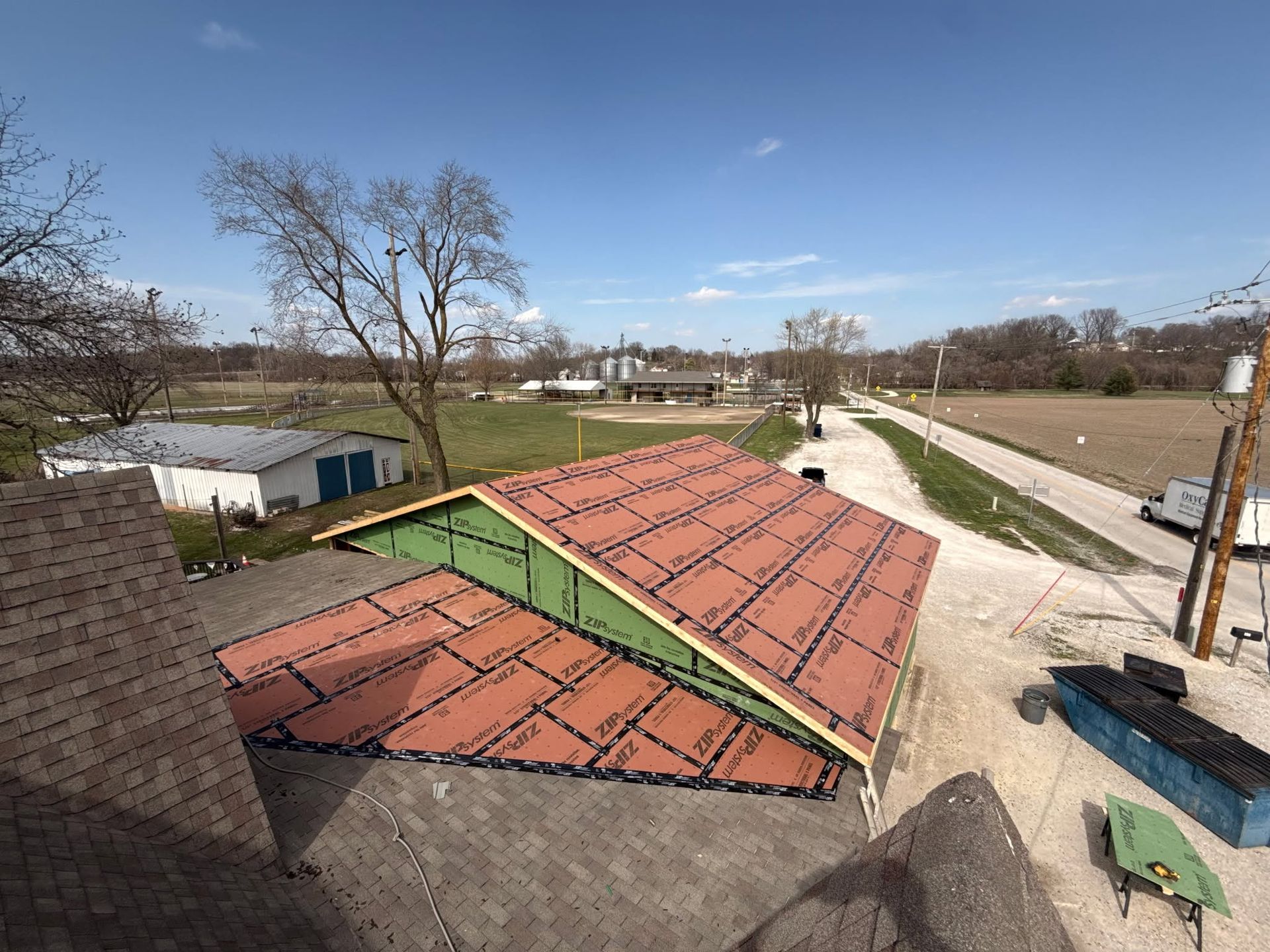 Rooftop with red shingles beside a paved path and open park under a clear blue sky