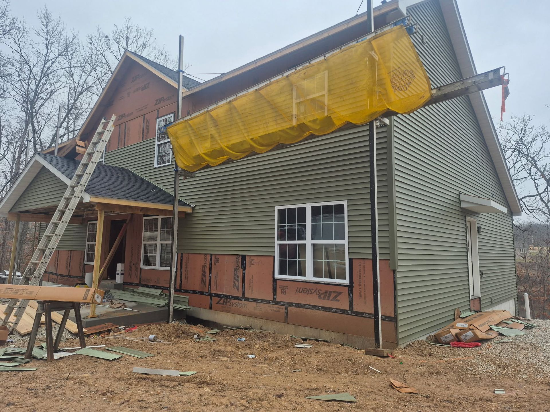 House under construction with scaffolding and yellow tarp on the roof, exterior siding in progress