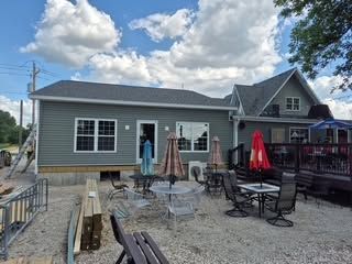 Patio with tables, umbrellas, and chairs beside a house under a cloudy sky
