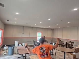 Person in orange shirt standing in a large room with tables, chairs, and a curved ceiling with recessed lights.