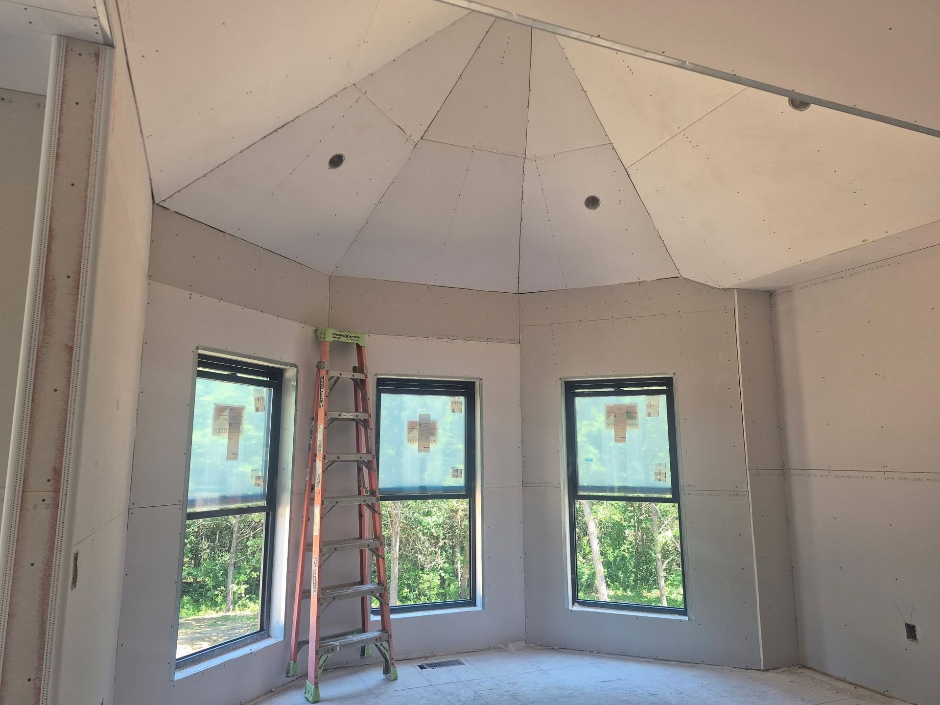 Unfinished room with a vaulted ceiling, three windows, and a ladder leaning against the wall.