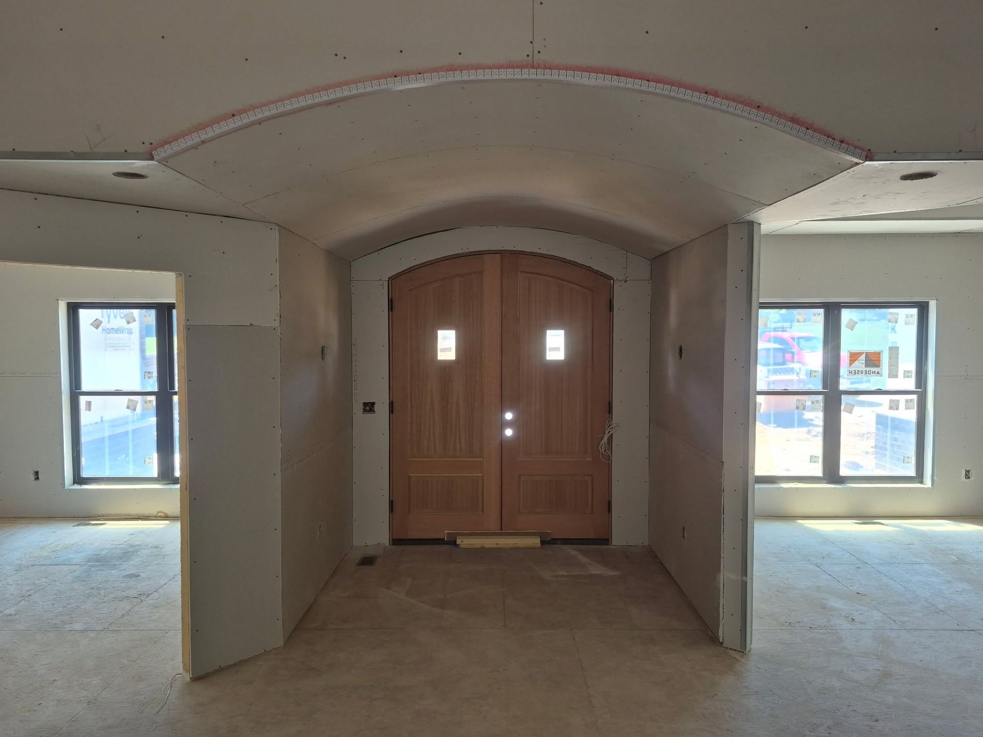 Unfinished interior room with arched ceiling, centered wooden double doors, and windows on both sides.