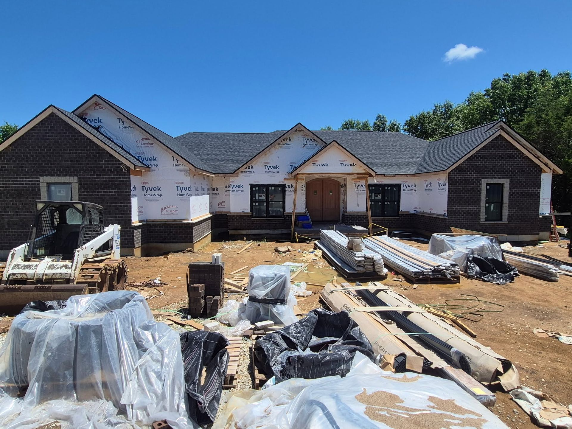 New house under construction with roof framing, wrapped materials, and building supplies on the ground