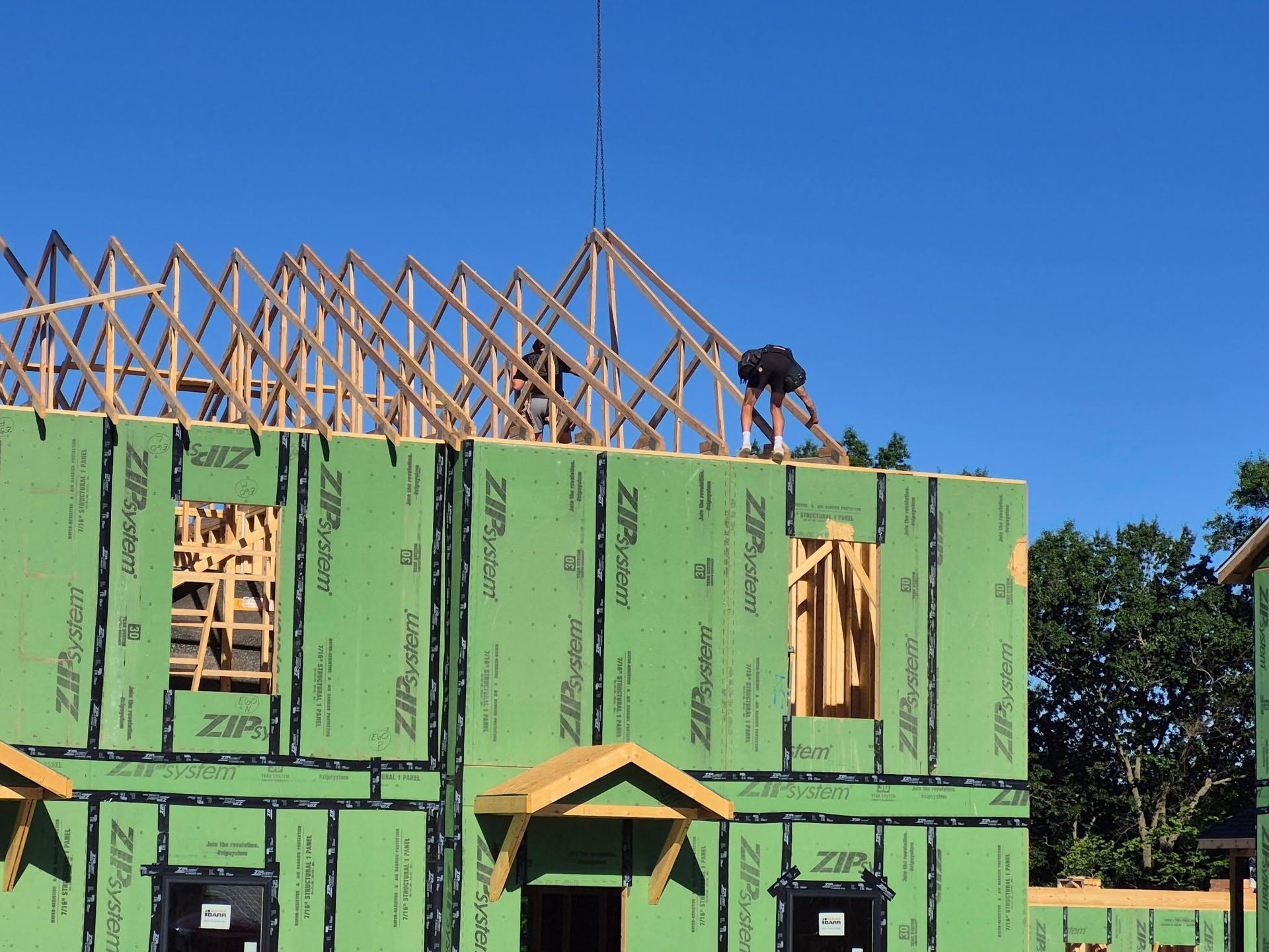 House under construction with green sheathing and exposed roof trusses against a blue sky