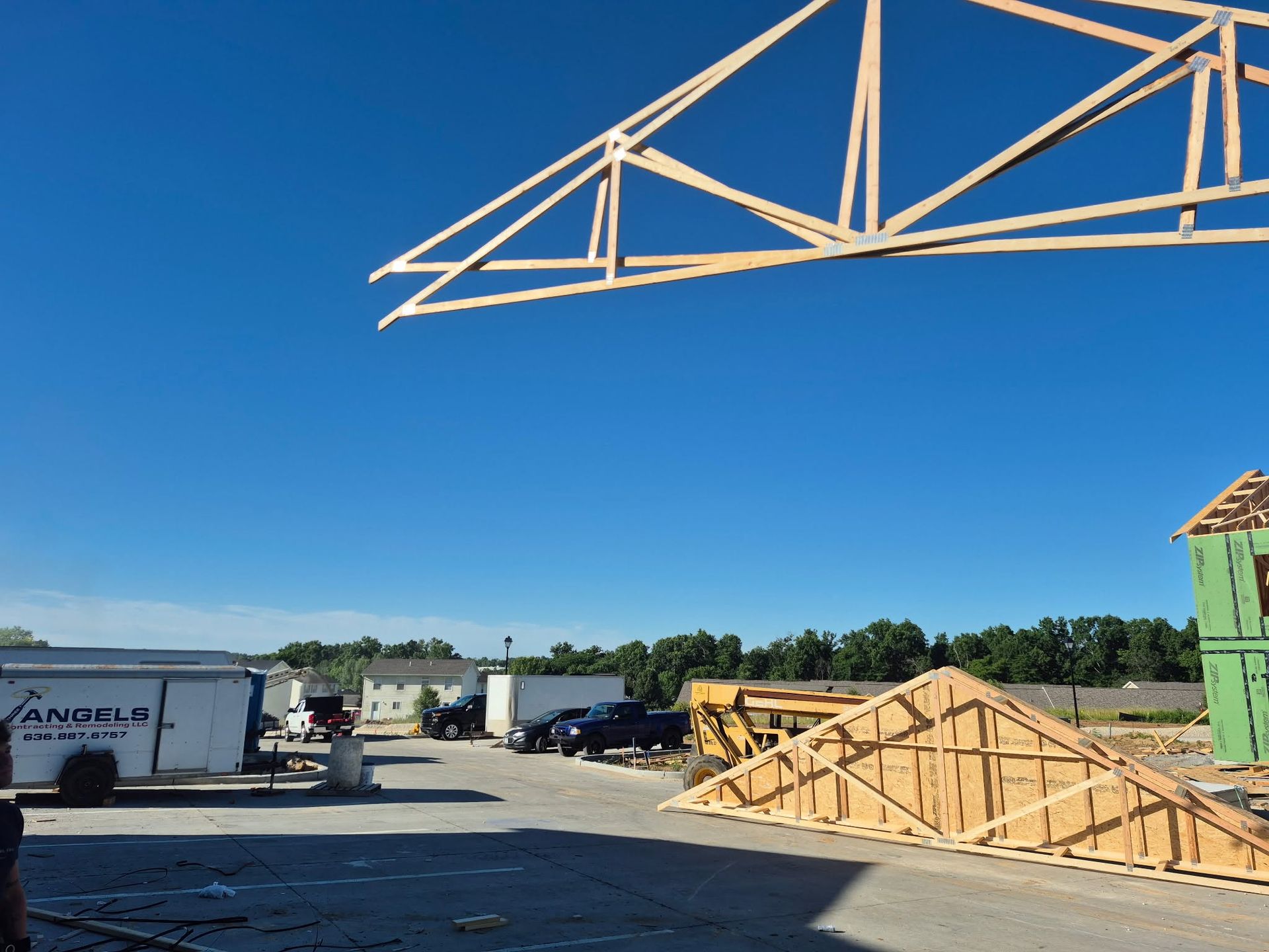 Construction site with crane truss overhead, lumber stacks, and trailers under a clear blue sky