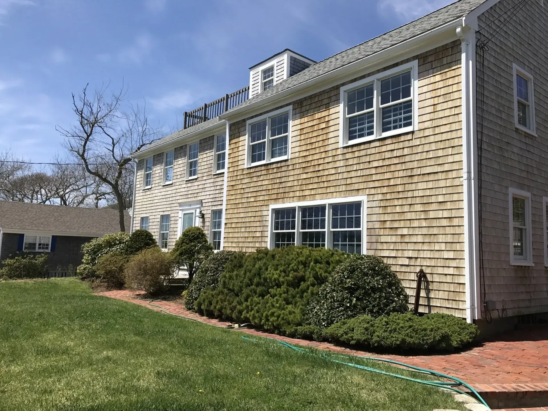 Two-story building with weathered wood siding, white-framed windows, and green landscaping under a bright sky.