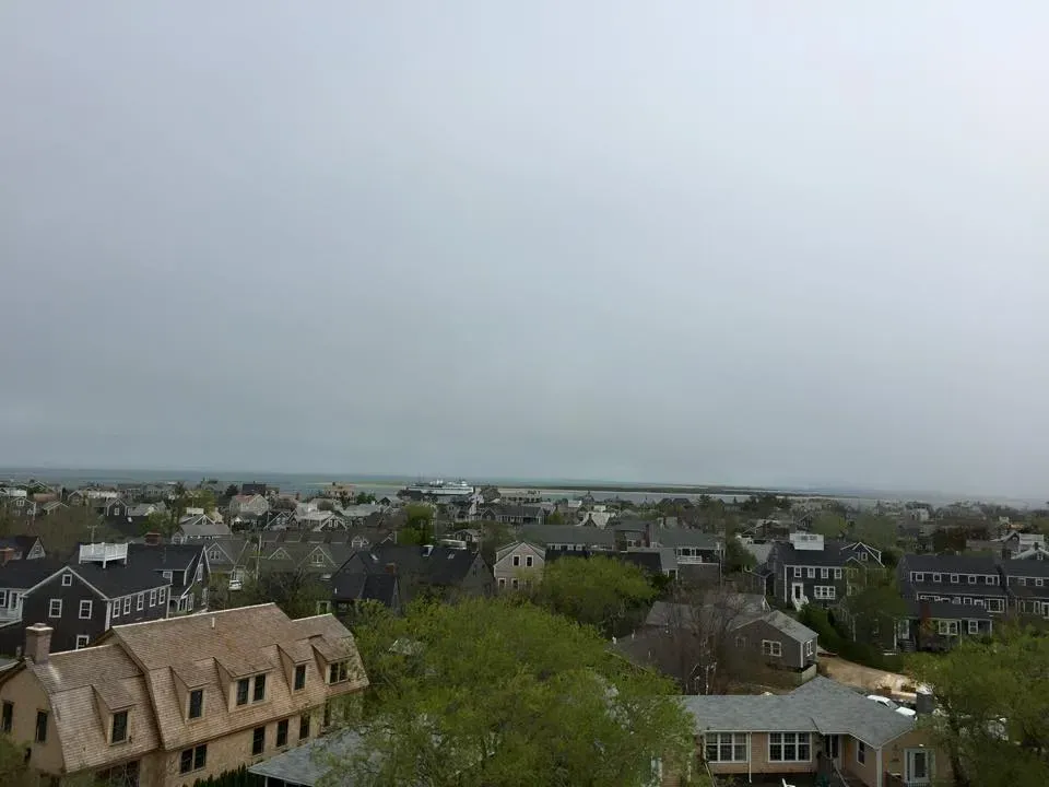 Overhead view of a town under a gray sky near the ocean. Houses and trees fill the scene.