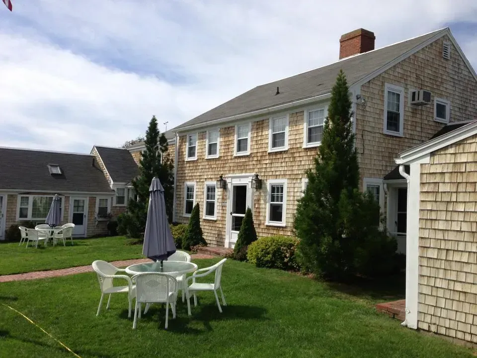 Buildings with wood shingle siding and white-framed windows, outdoor seating on a green lawn.