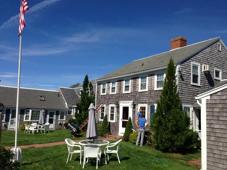 Buildings with weathered wood siding, lawn, patio furniture, and an American flag under a bright blue sky.