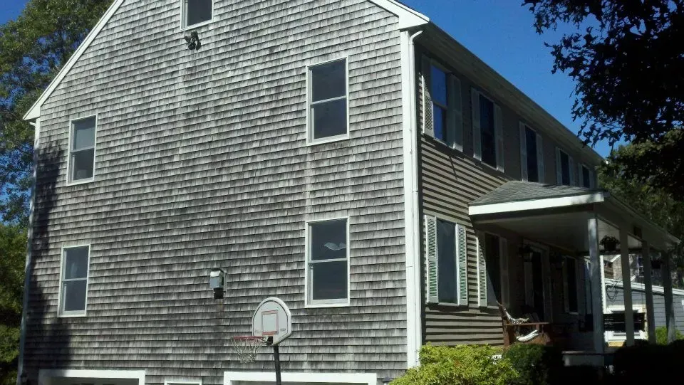 Two-story house with gray shingle siding, windows, and a small porch.