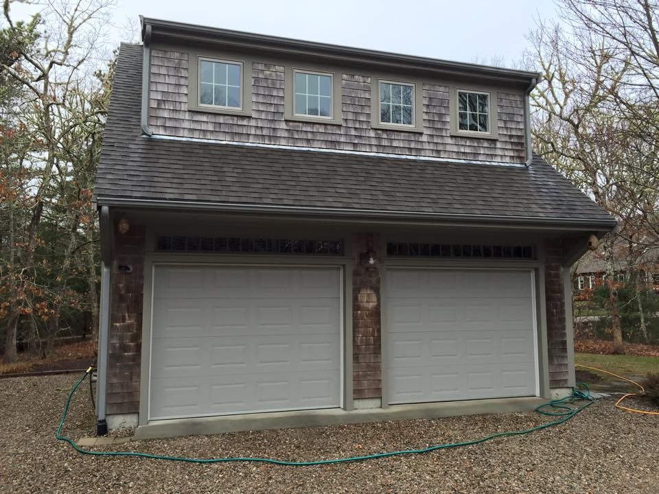 Two-car garage with a second-story dormer, cedar shake siding, and three windows.