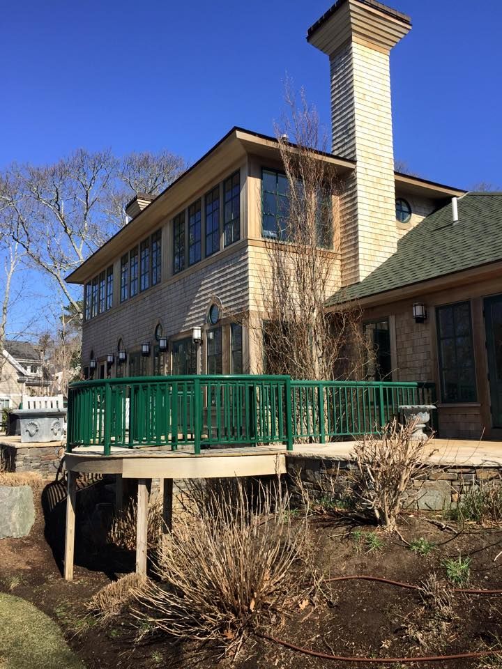 Exterior view of a multi-story home with a green-railed deck. Chimney and windows visible against a blue sky.