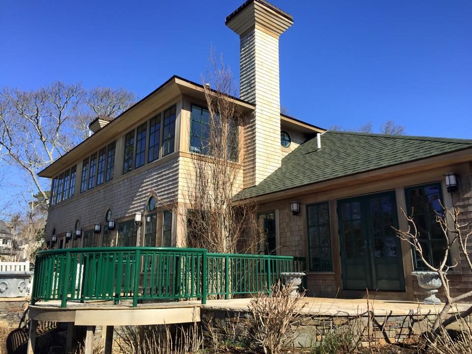 Two-story house with green deck railing, brick chimney, and green roof under a clear blue sky.