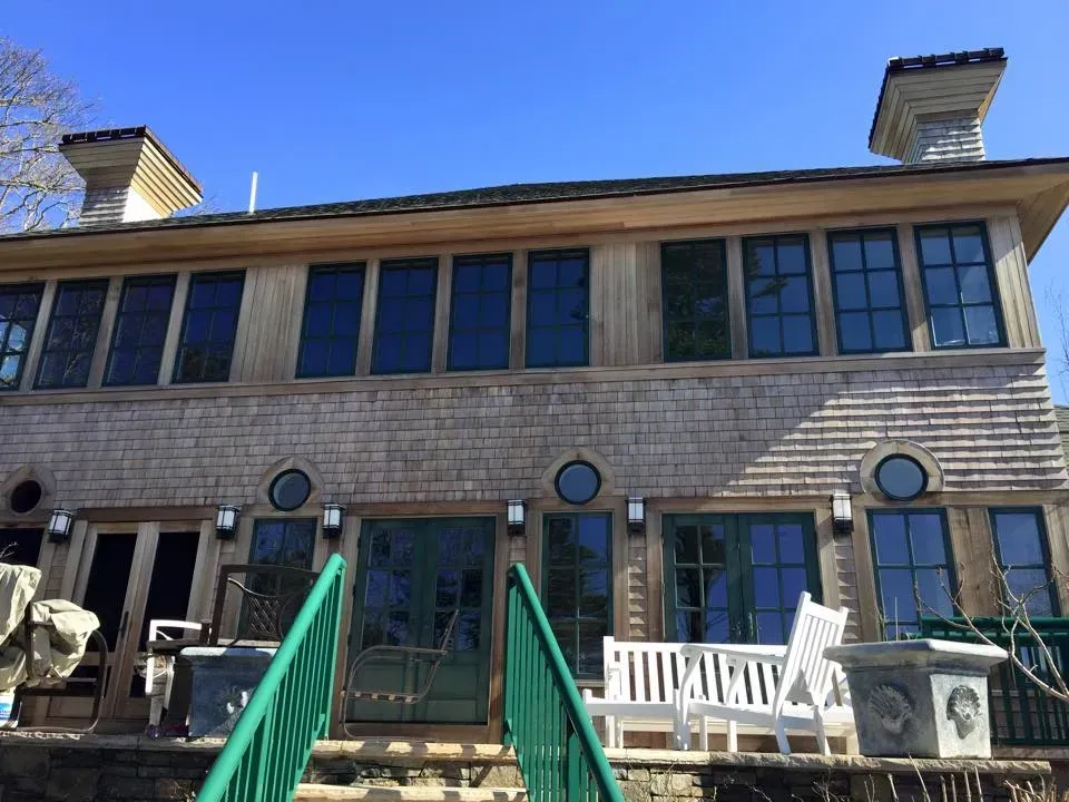 Wooden house with many windows and green trim, set against a bright blue sky.