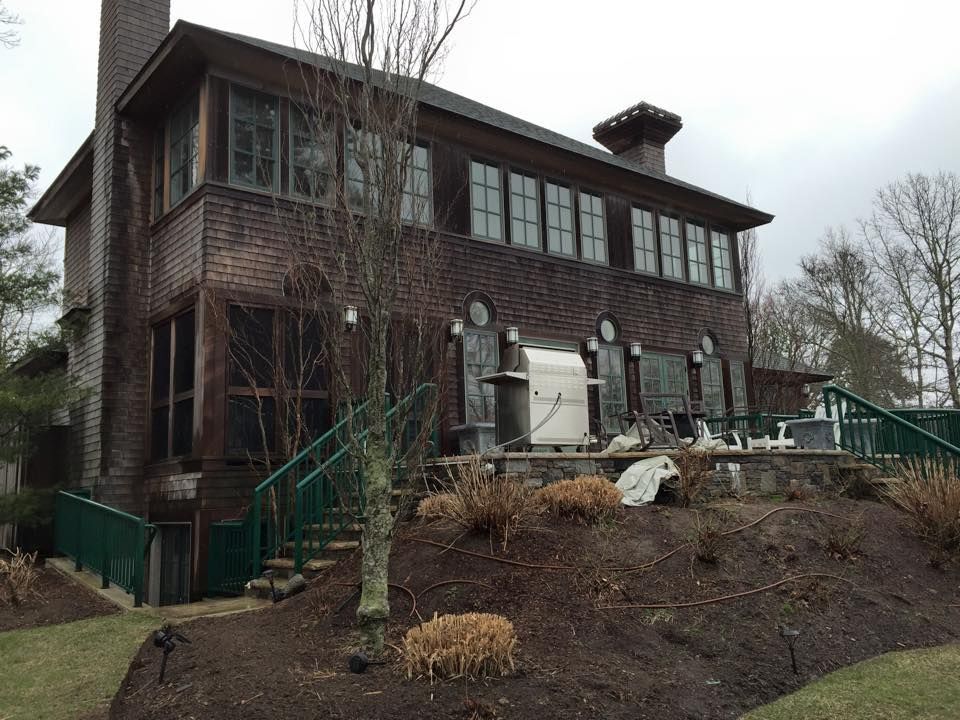 Brown brick house with multiple windows, chimneys, and a small deck with green railing.