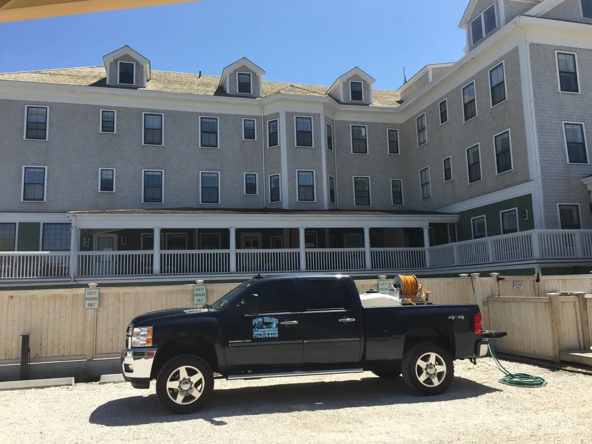 Black pickup truck parked in front of a light gray multi-story building with a light blue sky.