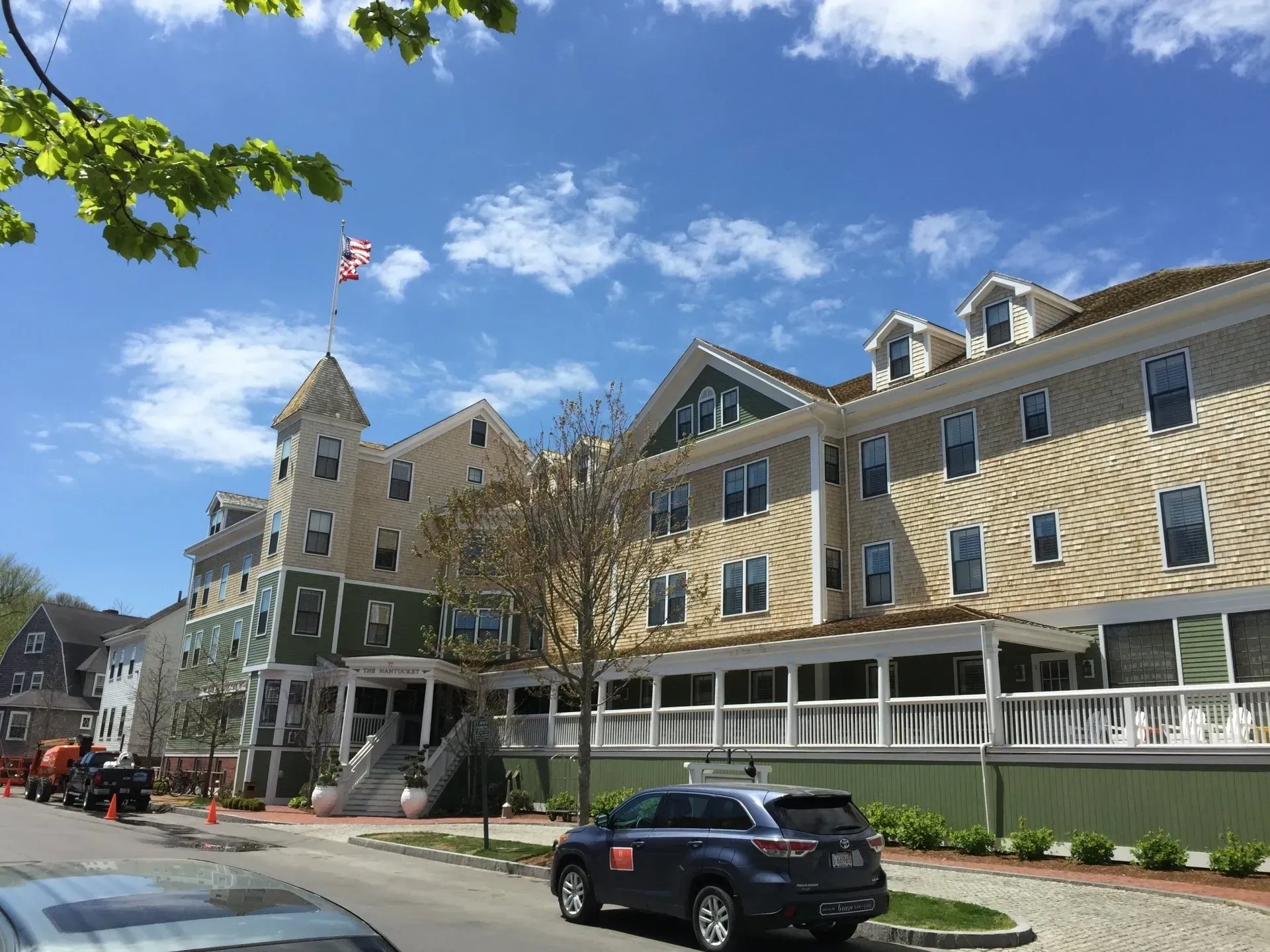 Multi-story building with green and tan siding, American flag on top, parked car, clear sky.