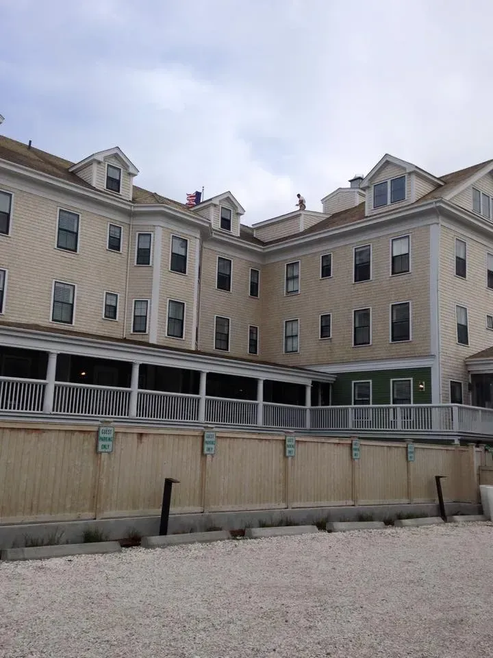 Cream-colored hotel with multiple windows, a porch, and a wooden fence; cloudy sky overhead.