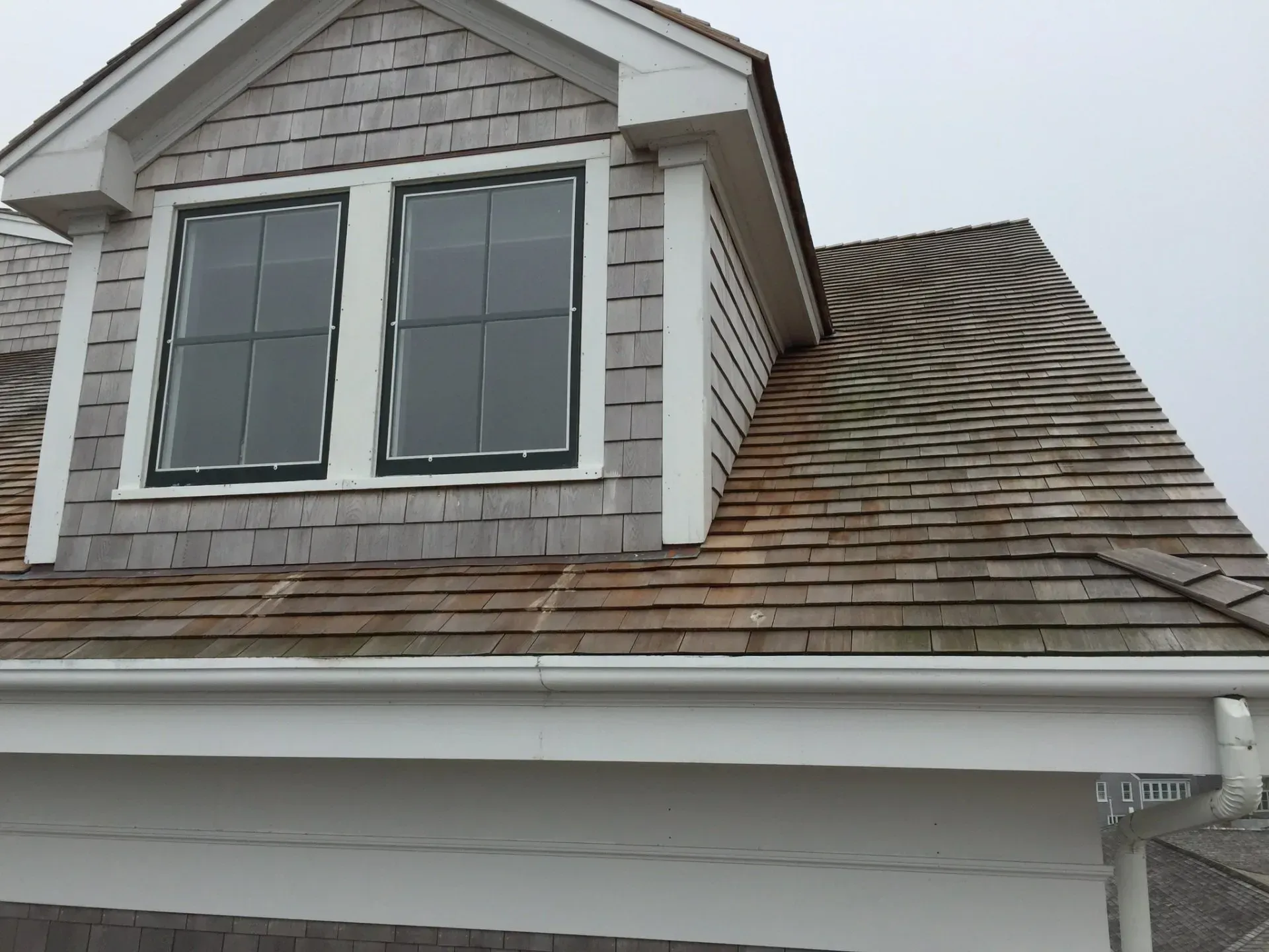 Dormer with two windows on a shingled roof, with white trim, and a white gutter along the eaves.