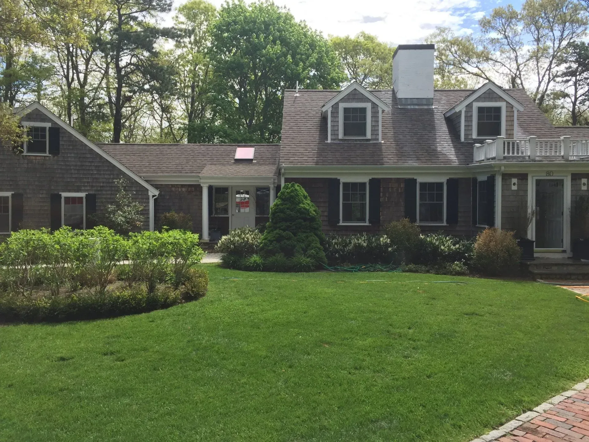 House with brown shingles, green lawn, white trim, and trees.